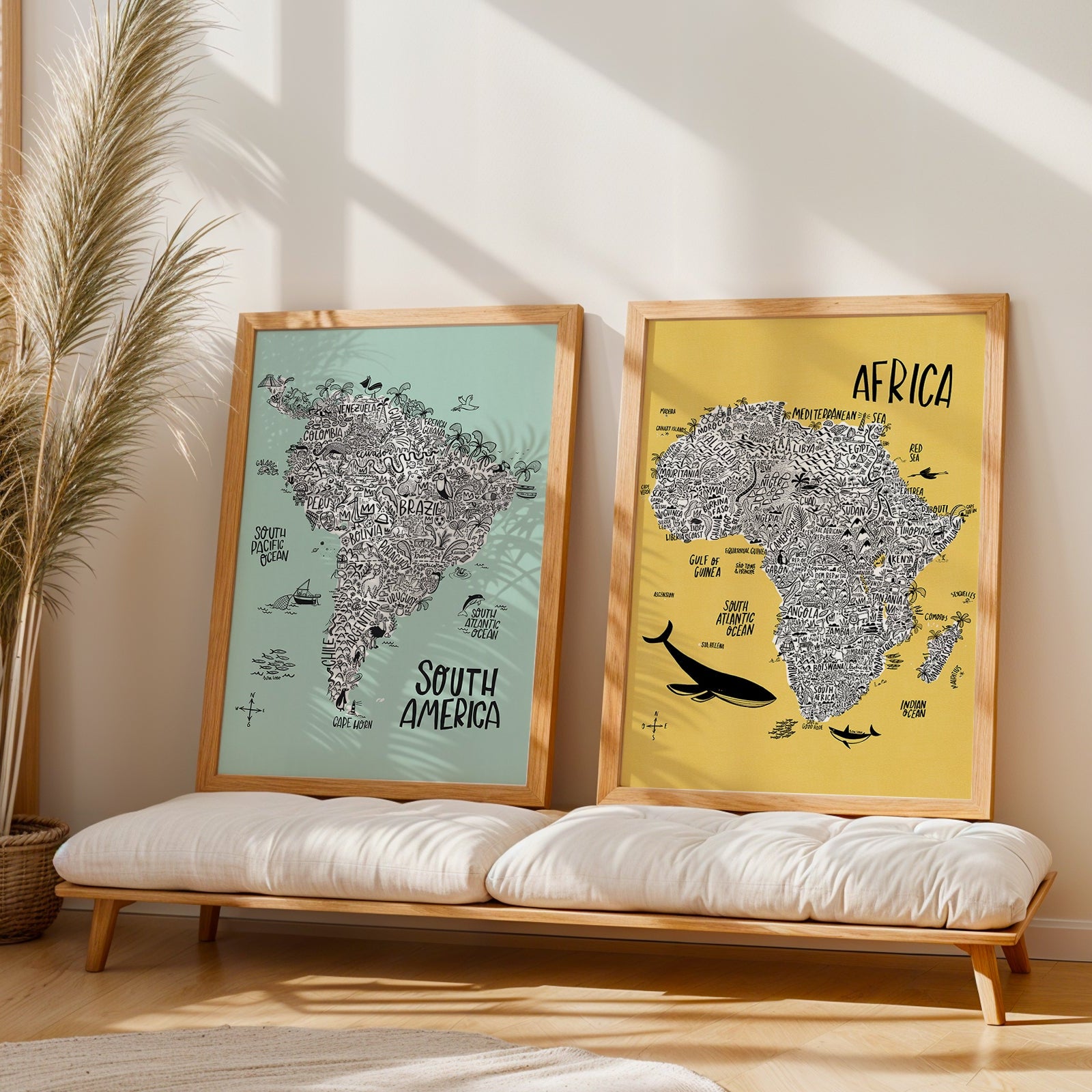 Two framed world maps of South America and Africa on a wooden bench with a plant in the background.