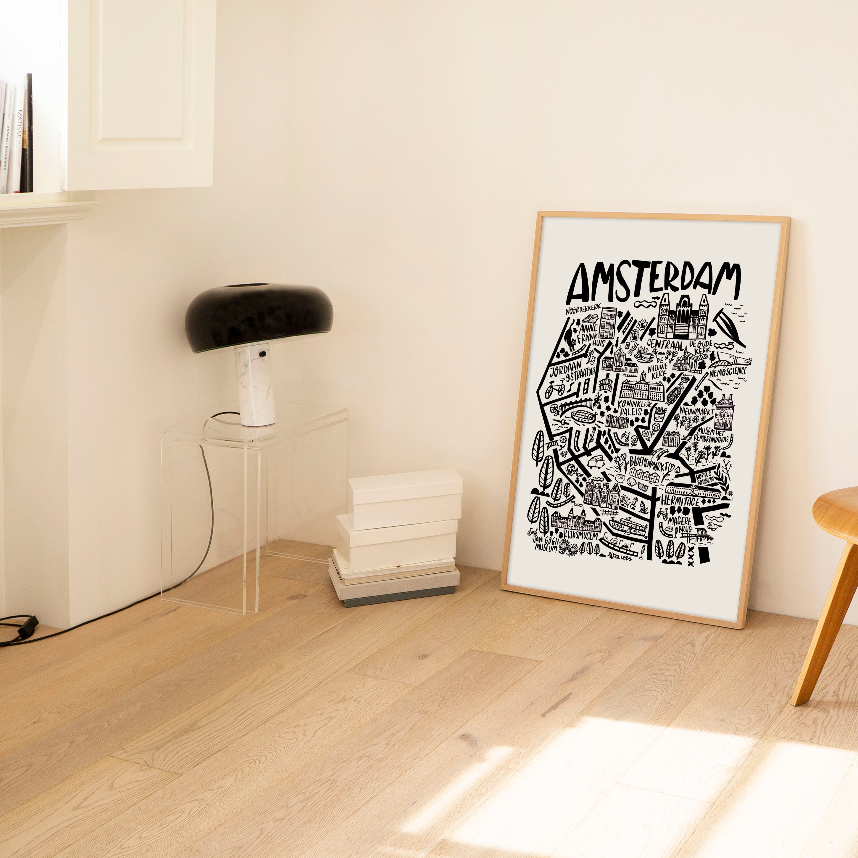 Framed Amsterdam map in a minimalistic room with a wooden chair and lamp.