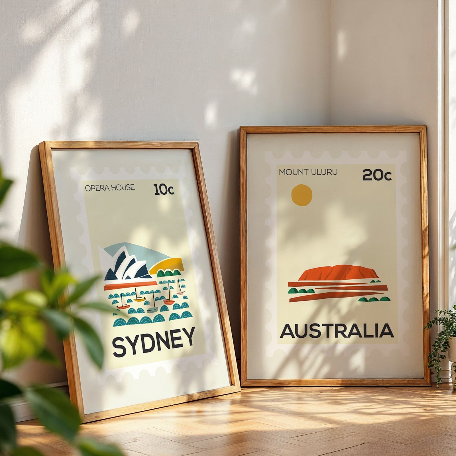 Two framed prints of Australian landmarks on a wooden floor with plants around.