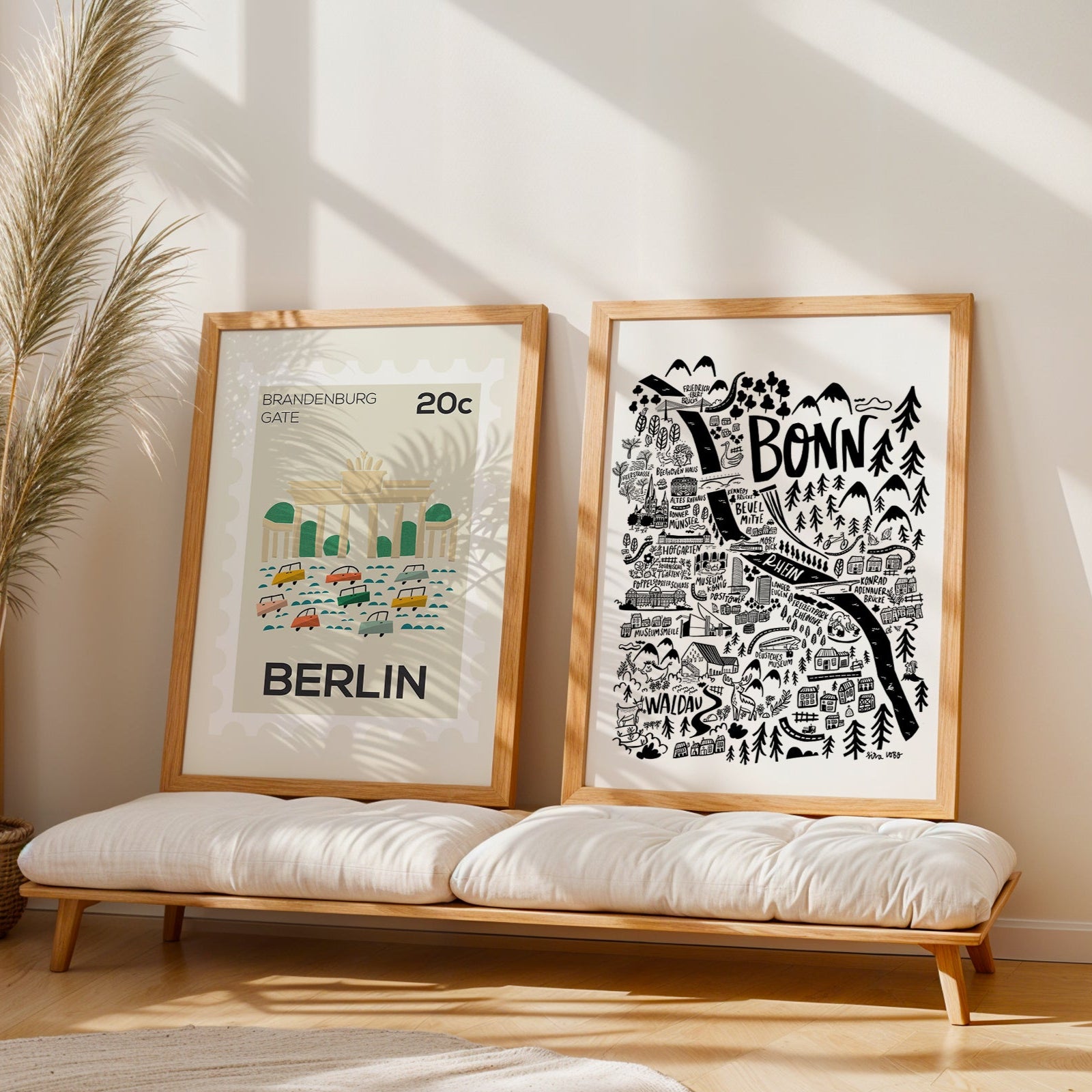 Two framed prints of Berlin and Bonn on a wooden bench with a plant in the background.
