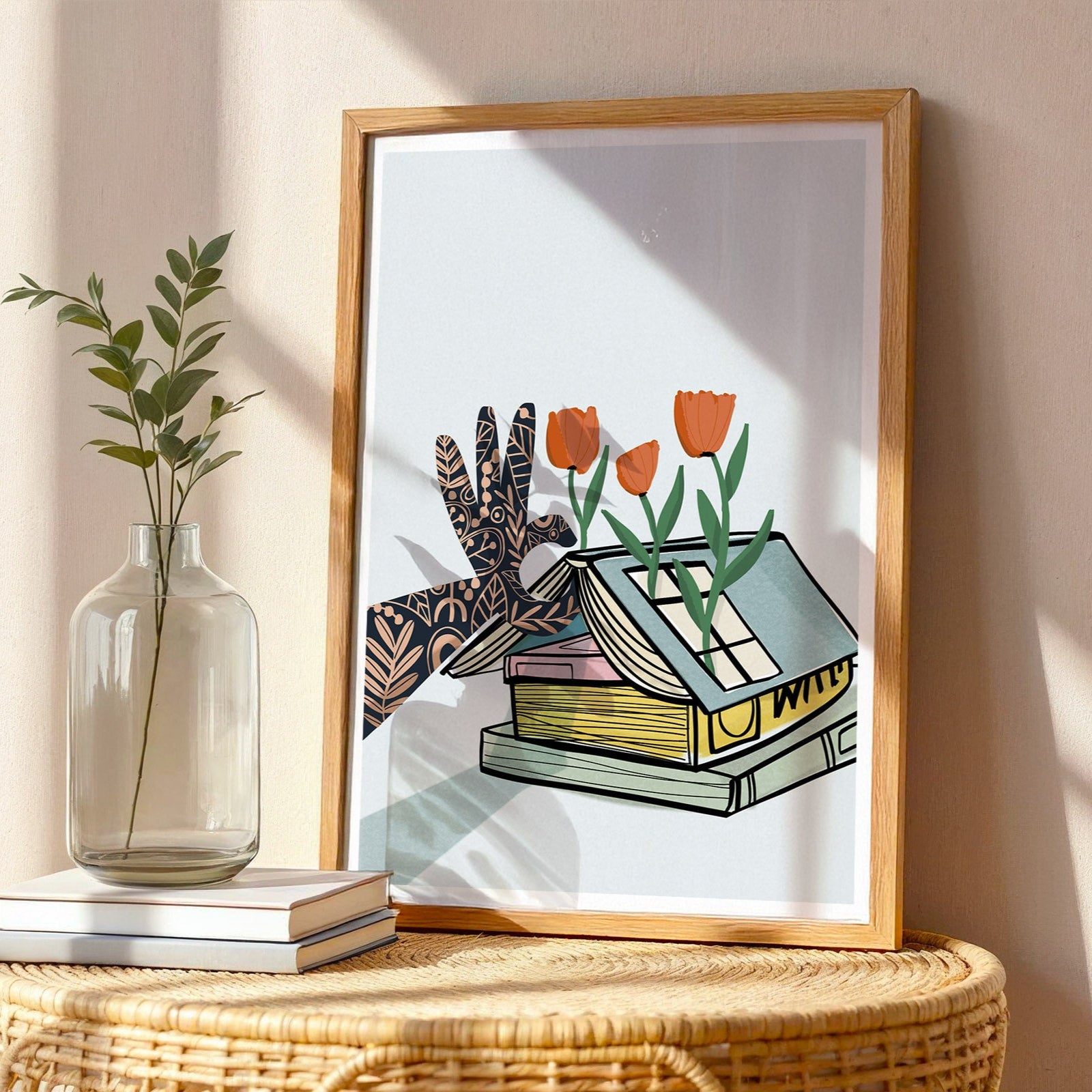 Framed artwork of a hand holding tulips next to books on a wicker table with a vase.
