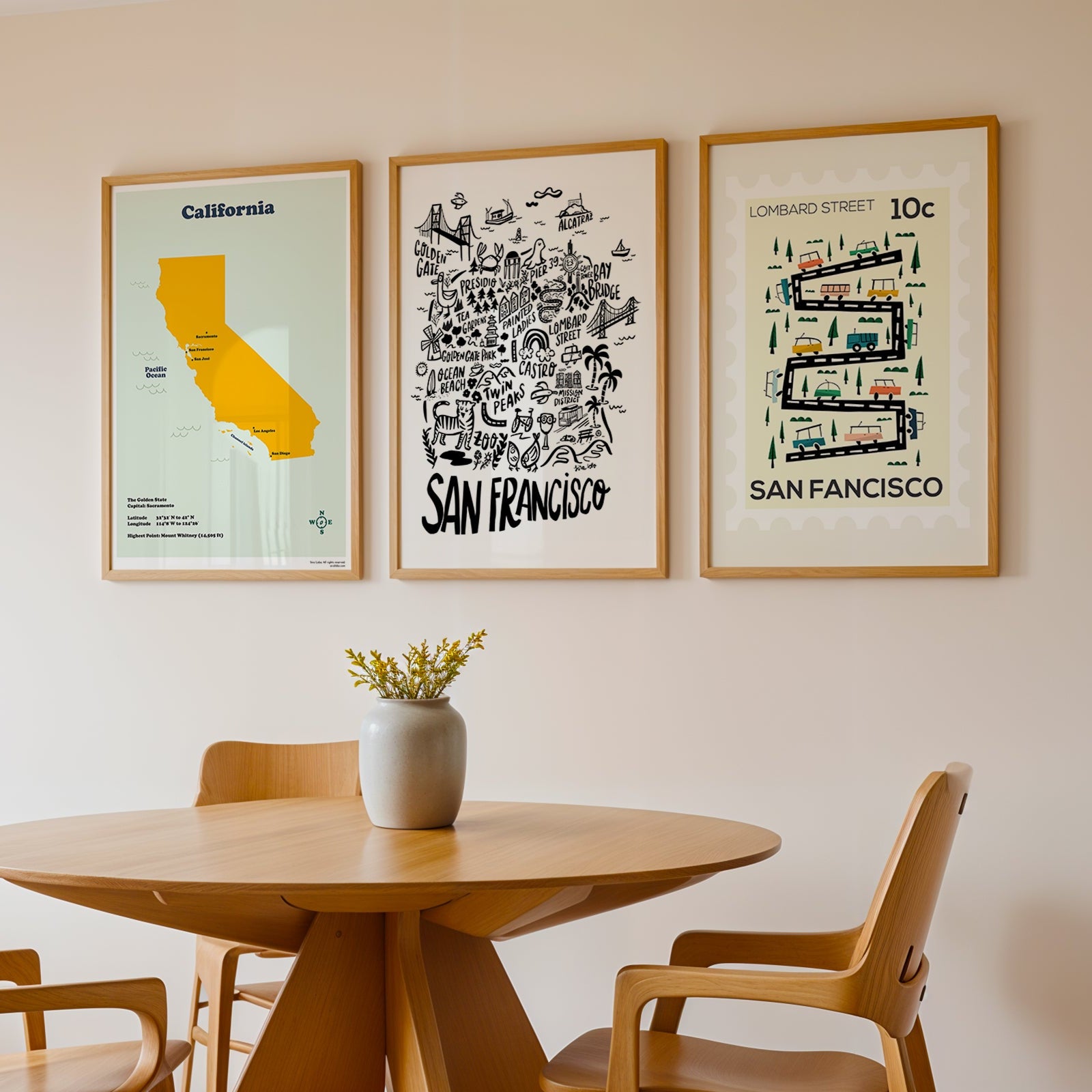 Framed posters of California and San Francisco on a wall above a wooden table with chairs.
