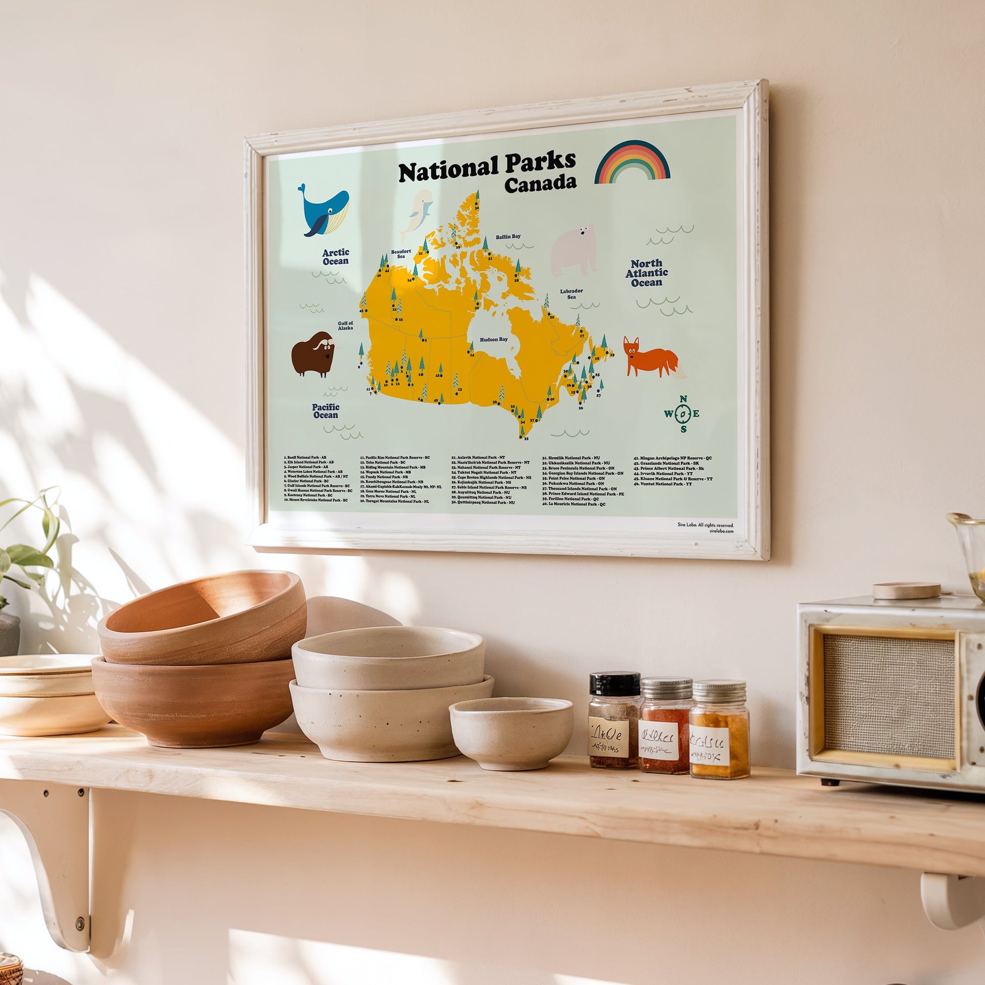 Framed map of National Parks in Canada on a wall above a wooden shelf with bowls and jars.