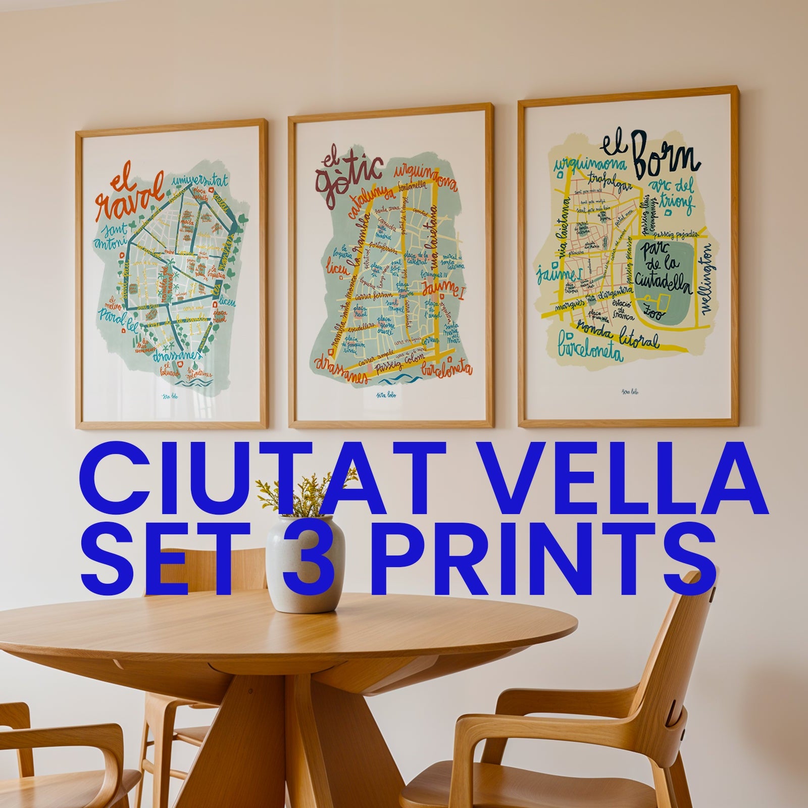 Three framed artworks on a wall above a wooden table with chairs.