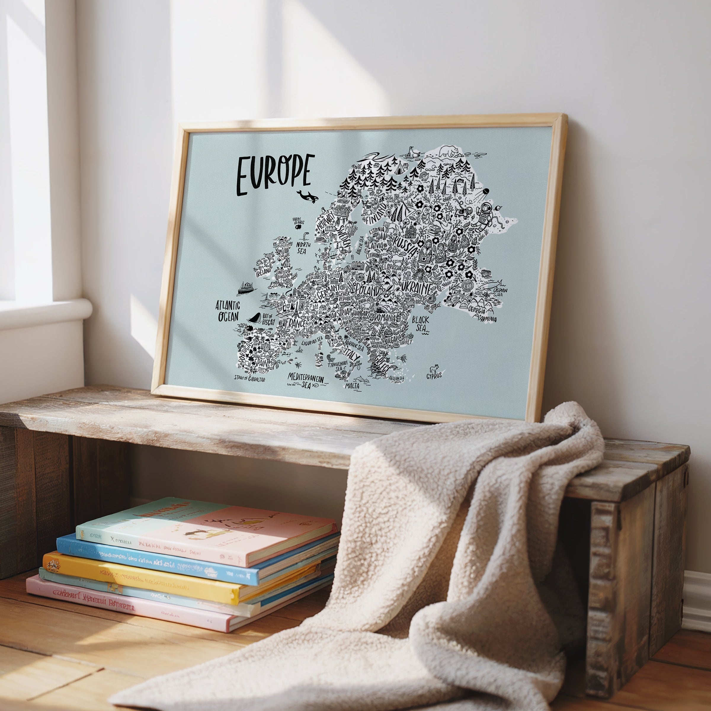 Framed map of Europe on a wooden shelf with books and a blanket.