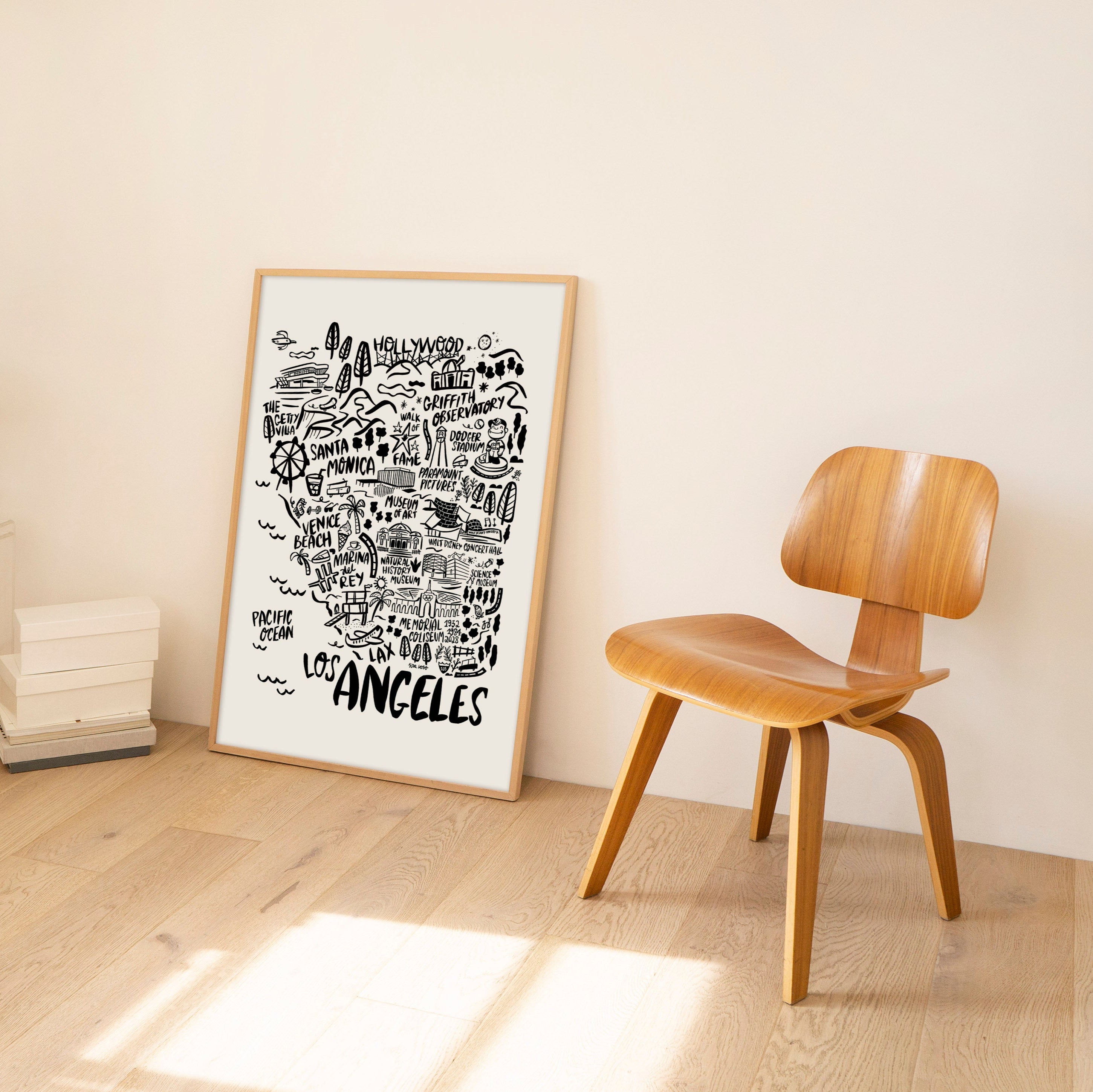 Framed map of Los Angeles on a wall with a wooden chair and modern lamp in a minimalistic room.