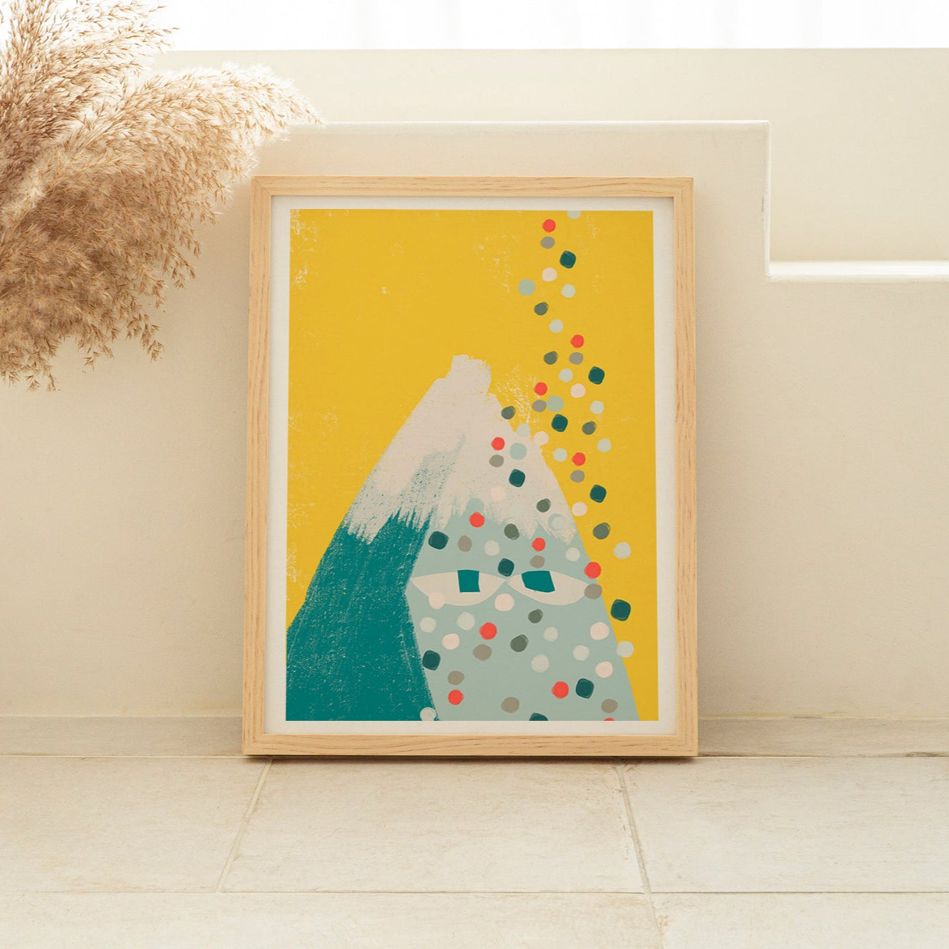 Framed artwork of a mountain with colorful dots on a yellow background, placed on a white surface.