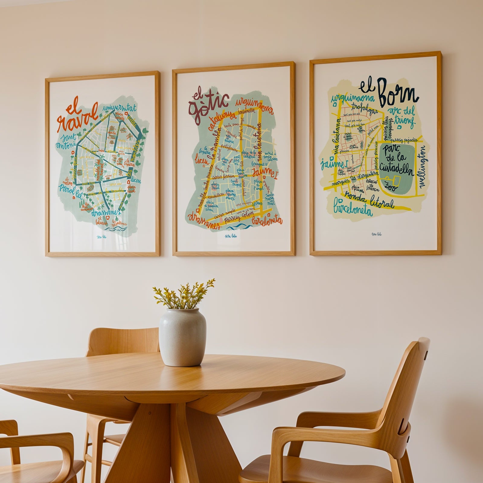 Three framed maps on a wall above a wooden table with chairs.