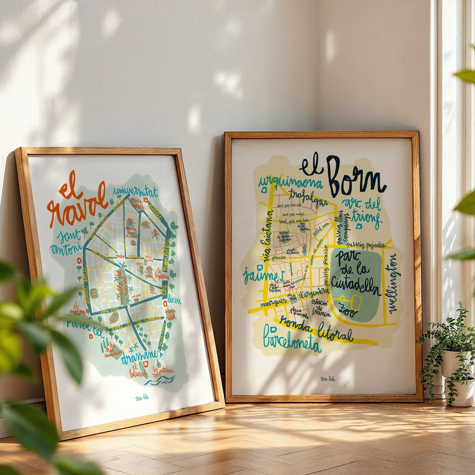 Two framed maps of El Born, a neighborhood in Barcelona, on a wooden floor with plants around.