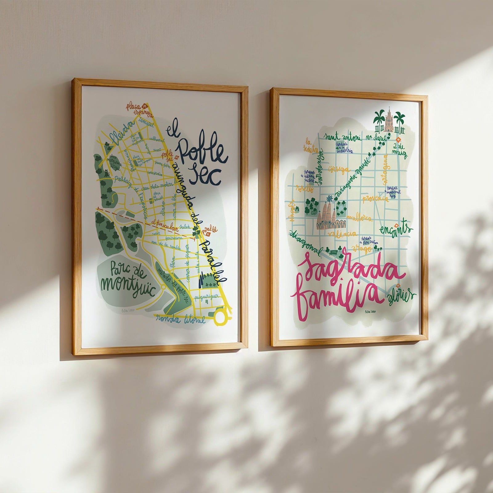 Two framed maps on a wall with sunlight casting shadows.