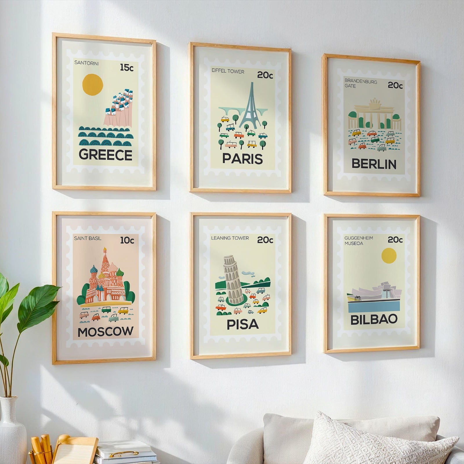 Framed posters of famous landmarks on a wall with a plant and sofa in the foreground.