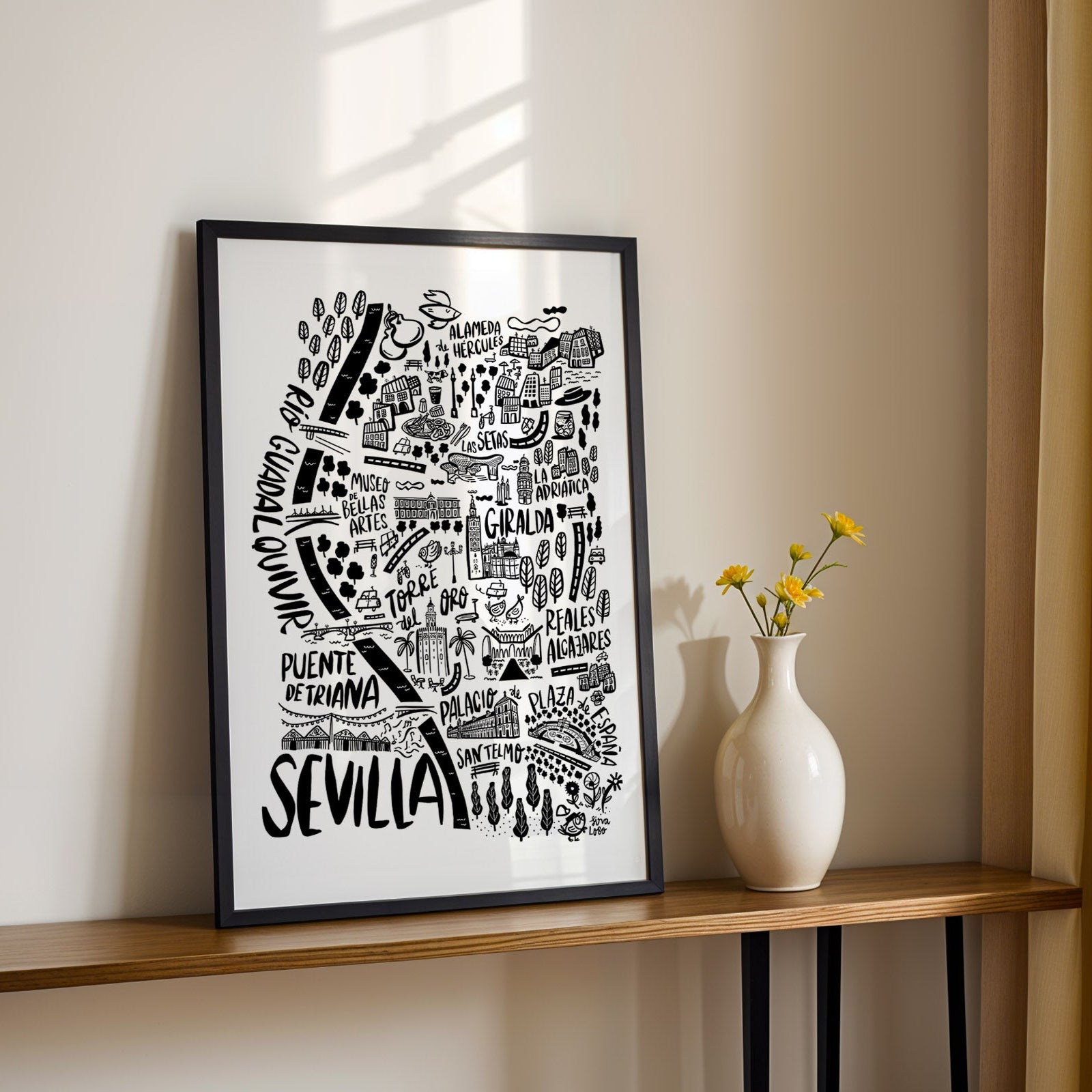 Framed black and white map of Sevilla on a wooden shelf with a vase and flowers.