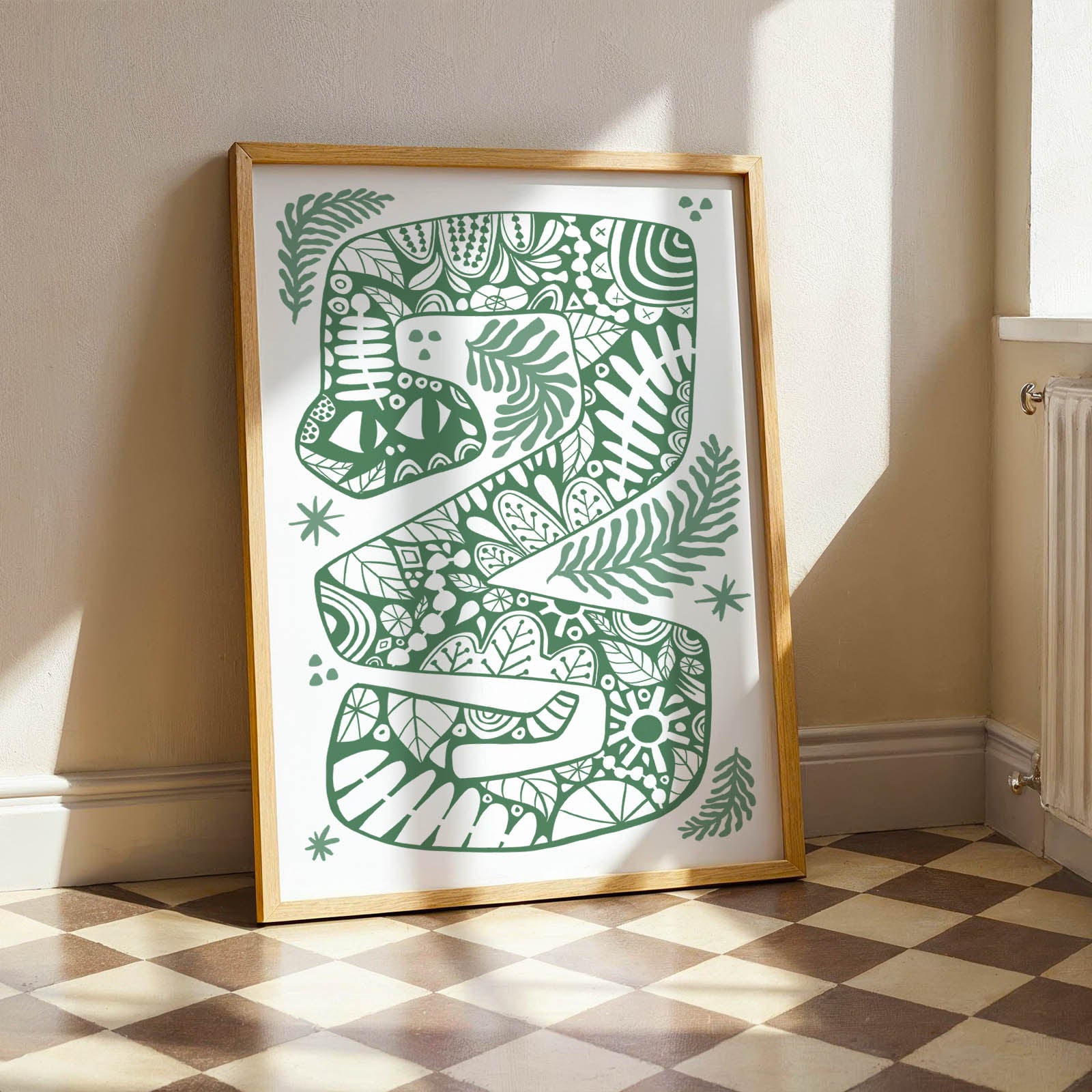 Framed artwork with a green snake design on a white background, leaning against a wall.