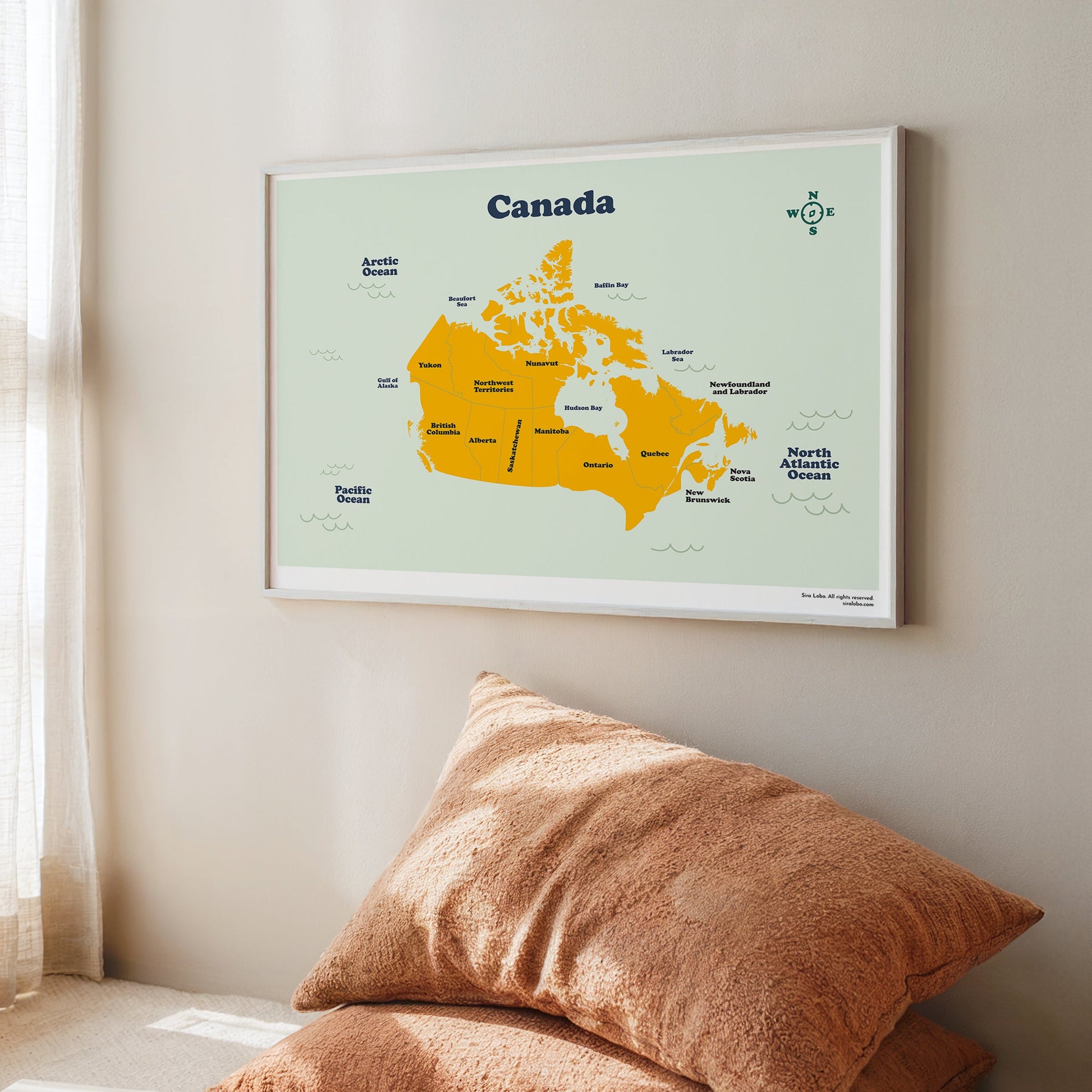 Framed map of Canada on a wall with two brown cushions in the foreground.