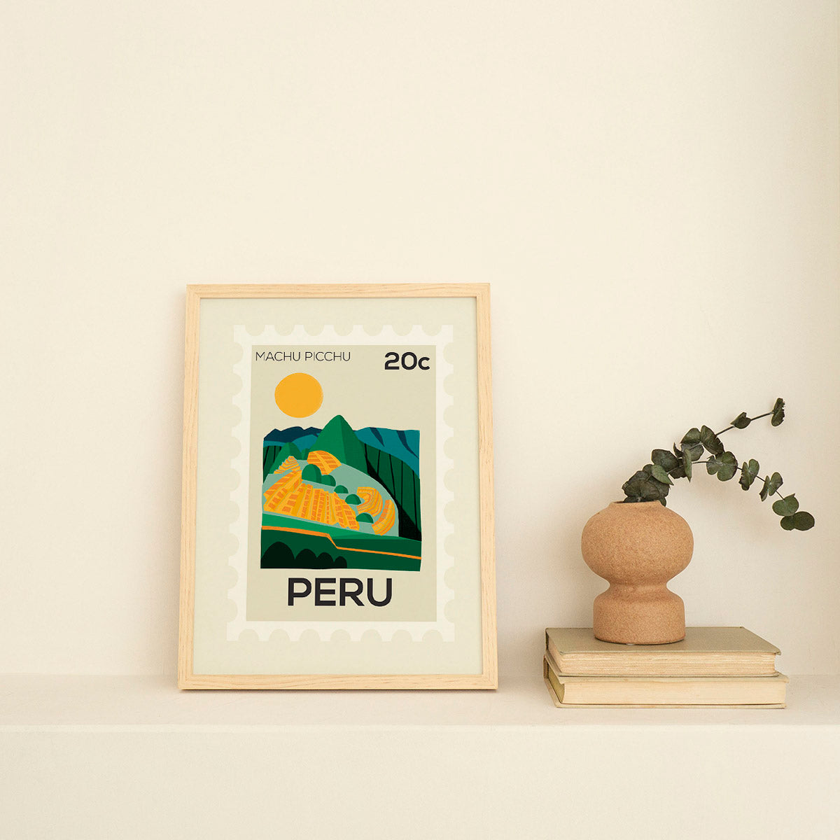 Framed artwork of Machu Picchu with a vase and books on a light background
