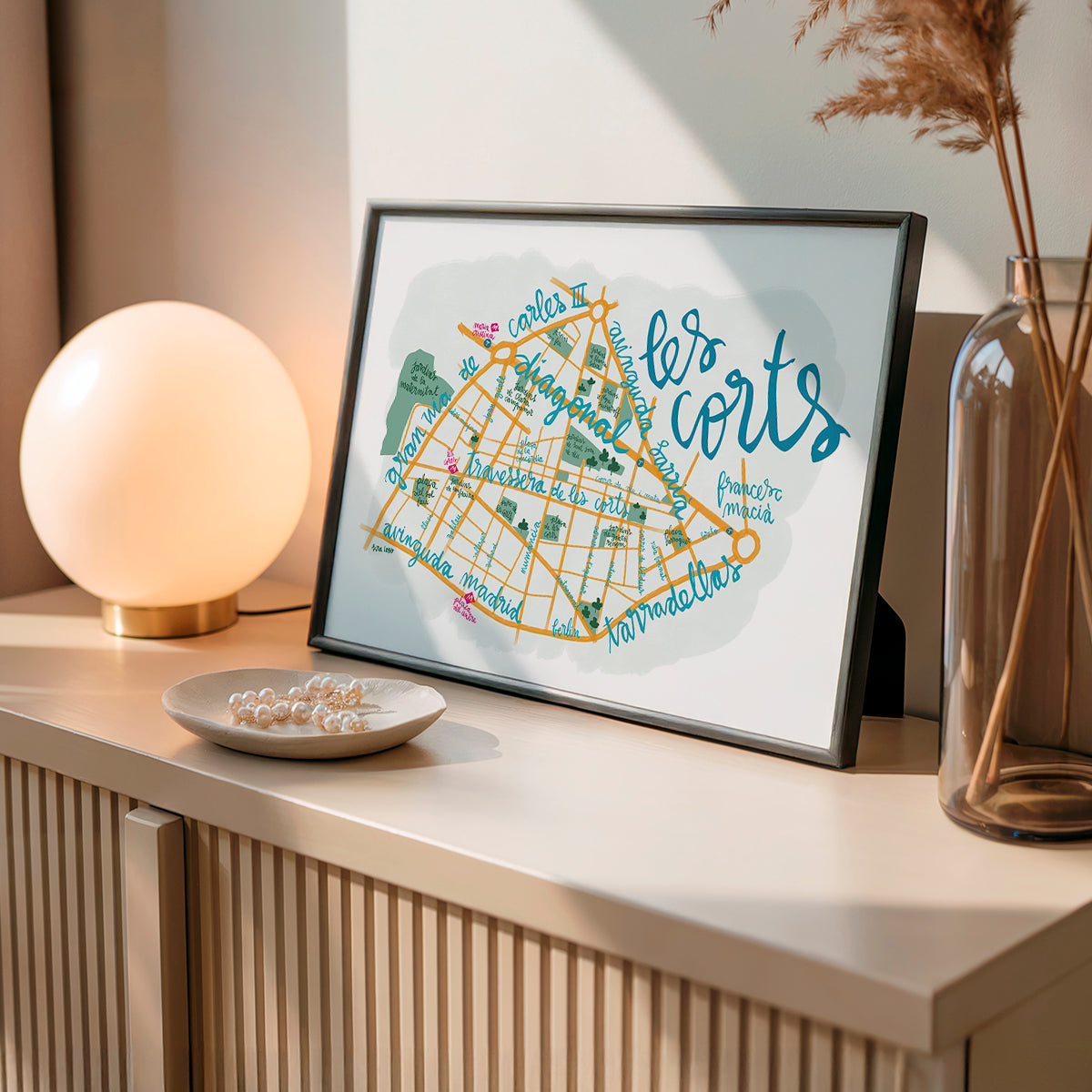 Framed map print of 'les corts' on a shelf with decorative items.