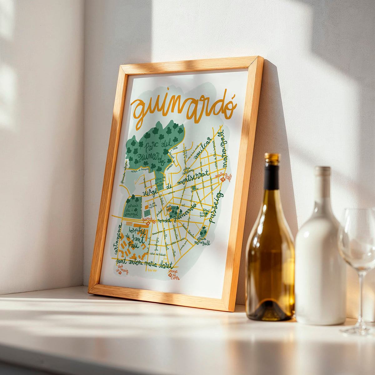 Framed map of Guinardó on a shelf with wine bottles and glasses.