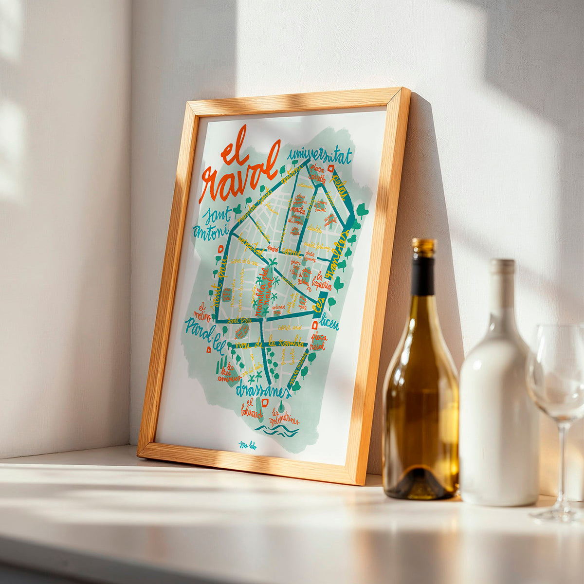 Framed map of El Raval neighborhood in Barcelona on a shelf with wine bottles and glasses.