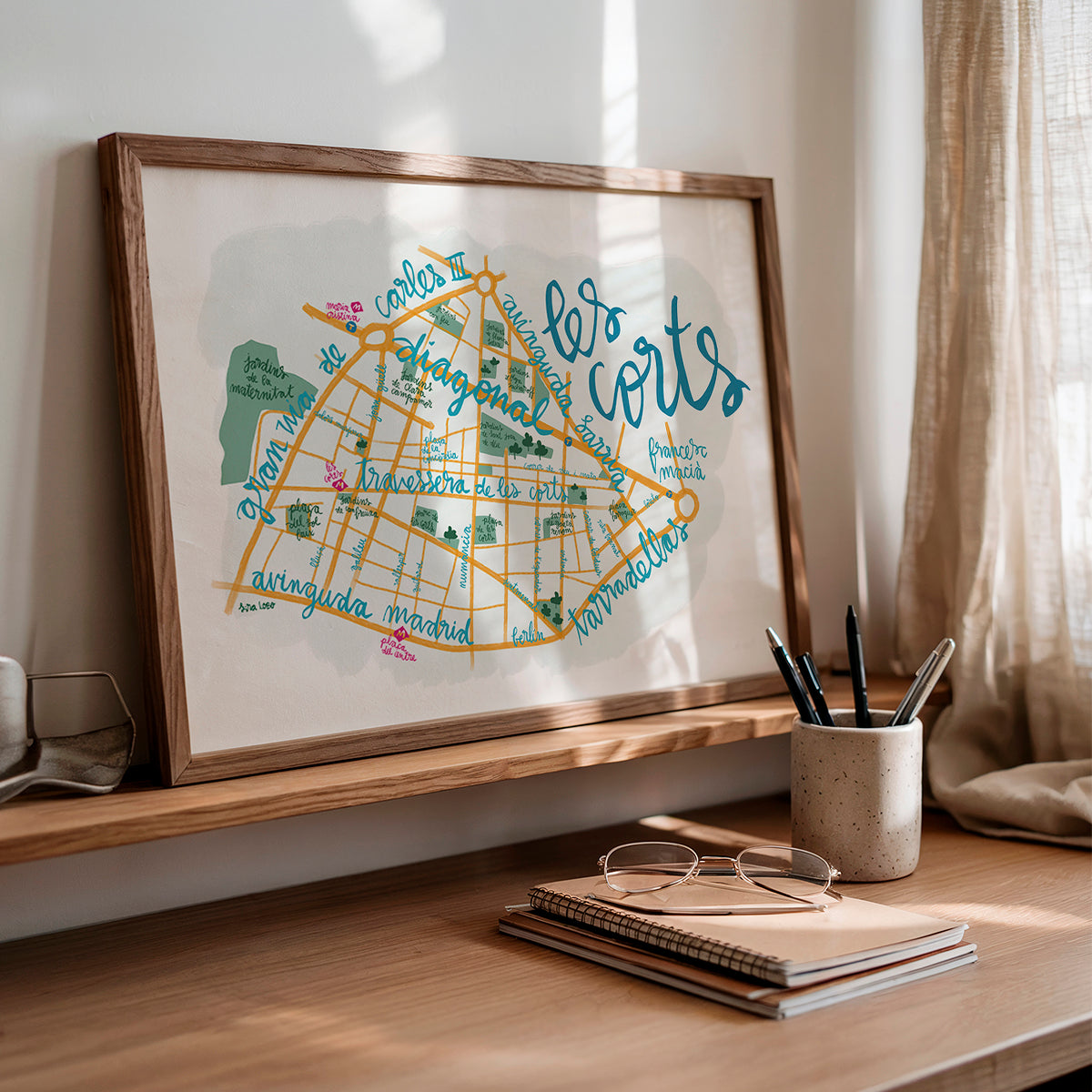 Framed map of 'Los Corts' on a wooden shelf with stationery items.