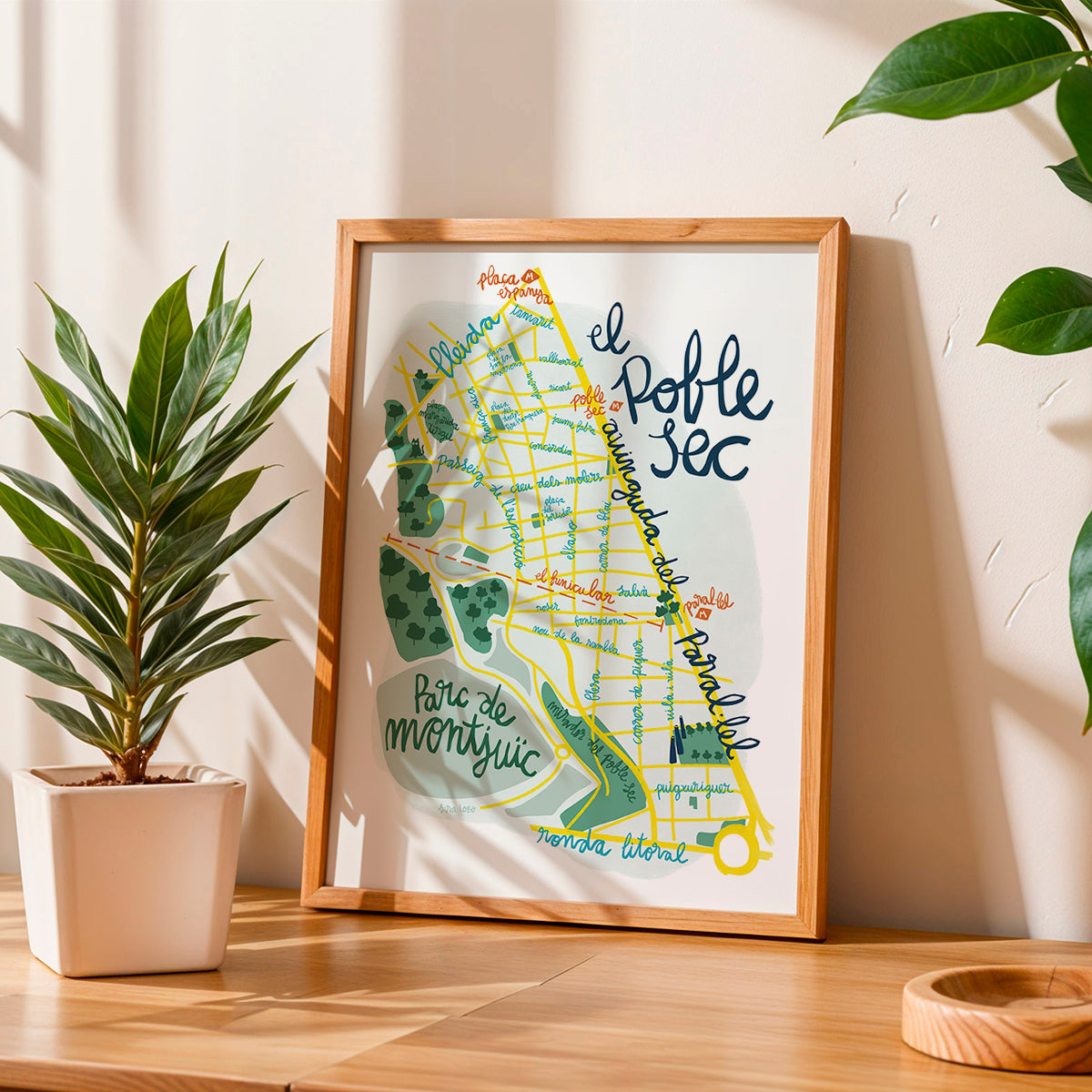 Framed map print of 'El Poble Sec' on a wooden surface with plants in the background