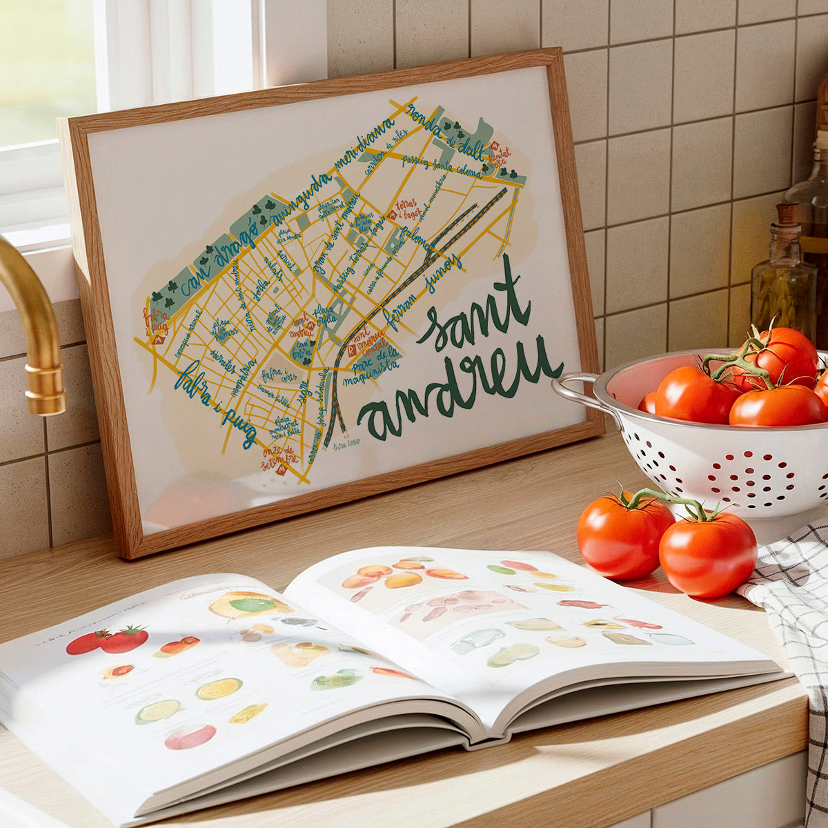 Framed map of Sant Andreu on a kitchen counter with an open book and tomatoes.