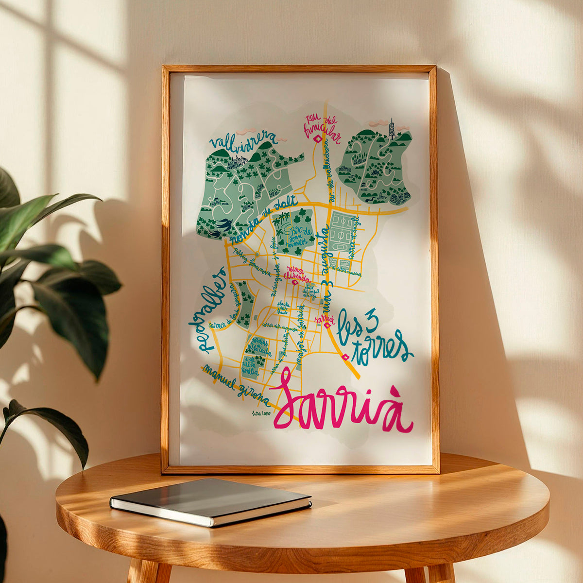 Framed colorful map of Sarrià in Barcelona on a wooden table with a plant in the background