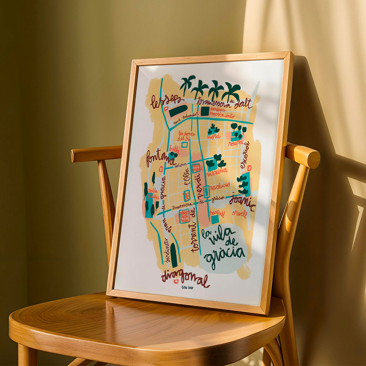 Framed map of Vila de Gràcia in Barcelona on a wooden chair against a green wall