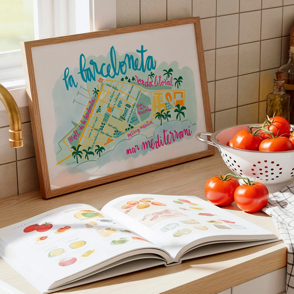 Framed map of Barcelona on a kitchen counter with an open book and tomatoes.