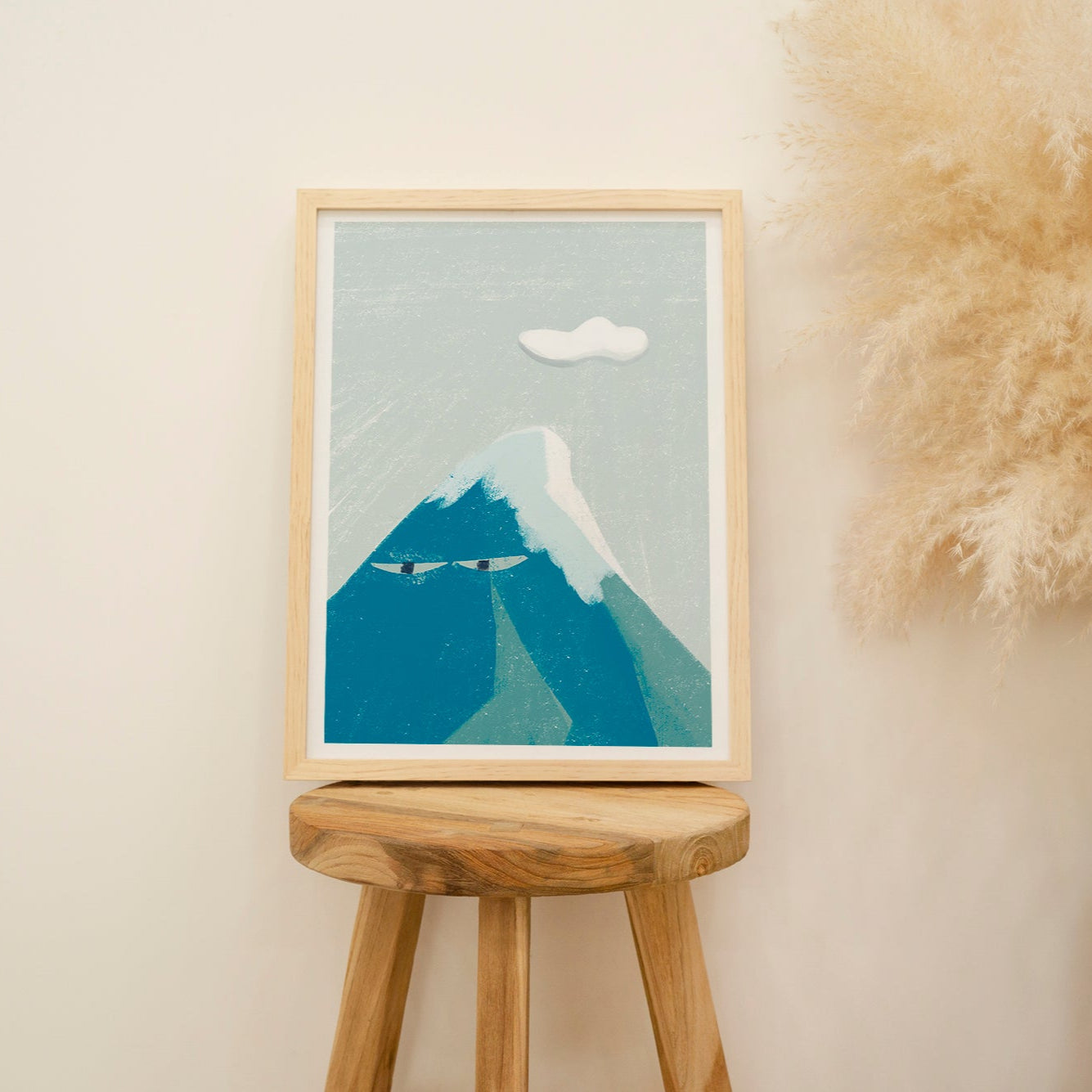 Framed artwork of a mountain on a wooden stool against a beige wall with decorative elements.