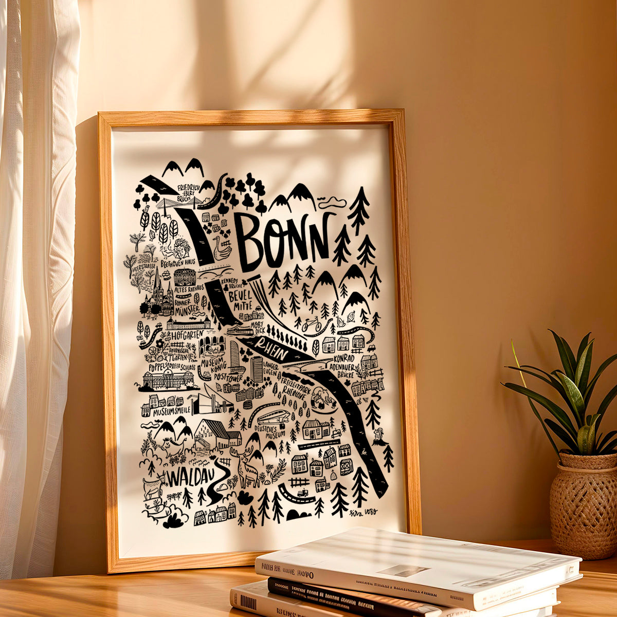 Framed map of Bonn on a table with books and a plant