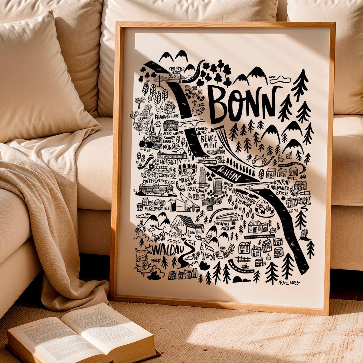 Framed map of Bonn with a beige sofa and open book in the background