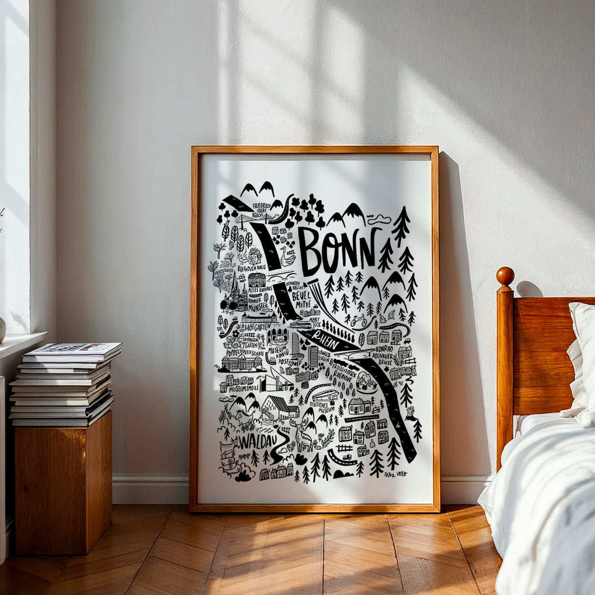 Framed map of Bonn in a bedroom with wooden bed and books.