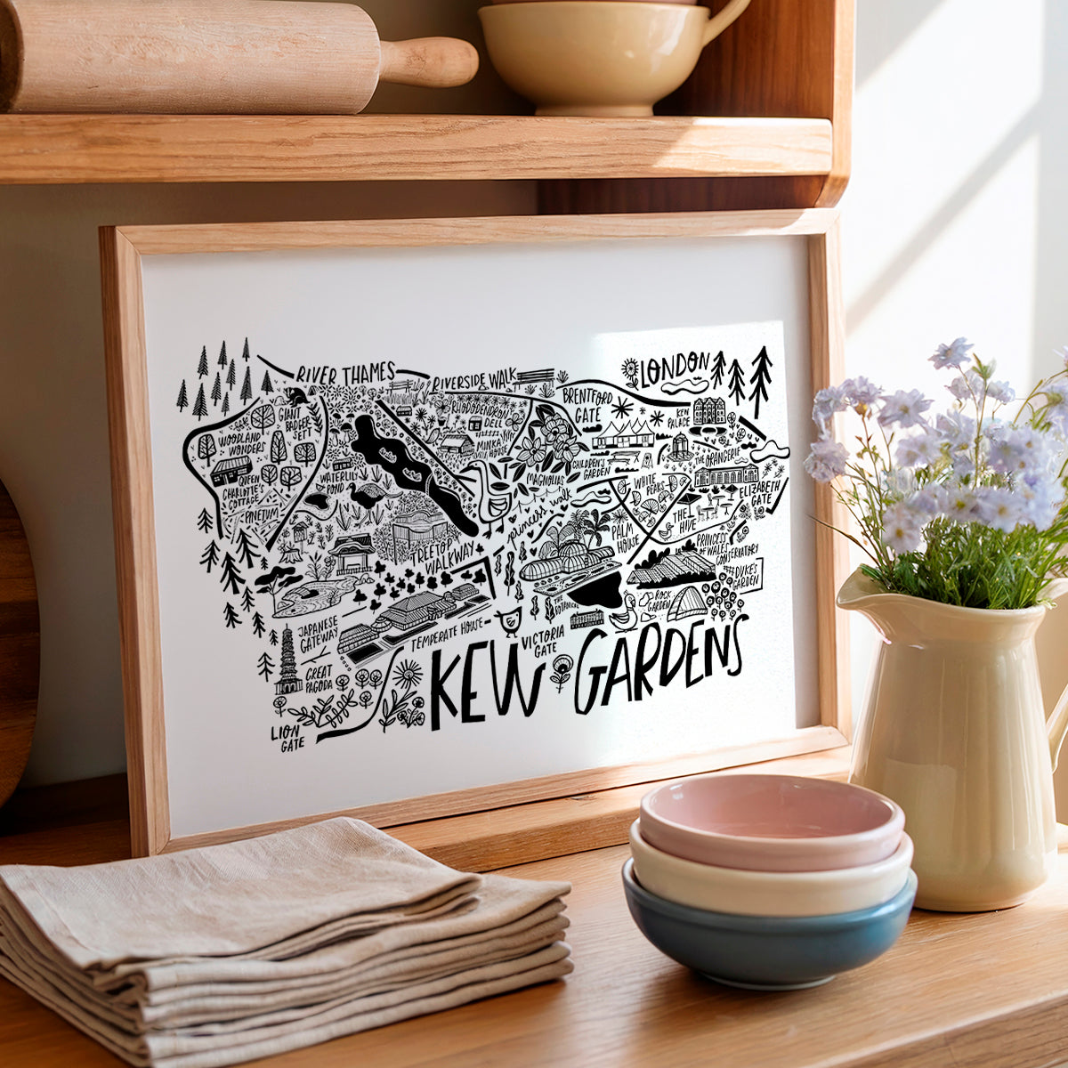 Framed map of Kew Gardens on a wooden shelf with kitchen items and flowers.