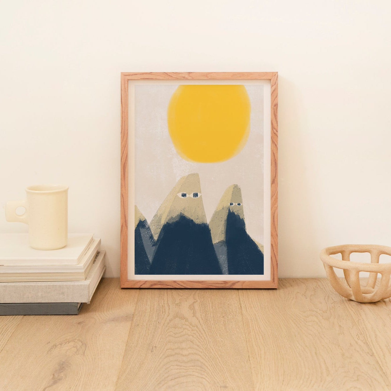 Framed artwork of two mountains under a yellow sun on a wooden floor.