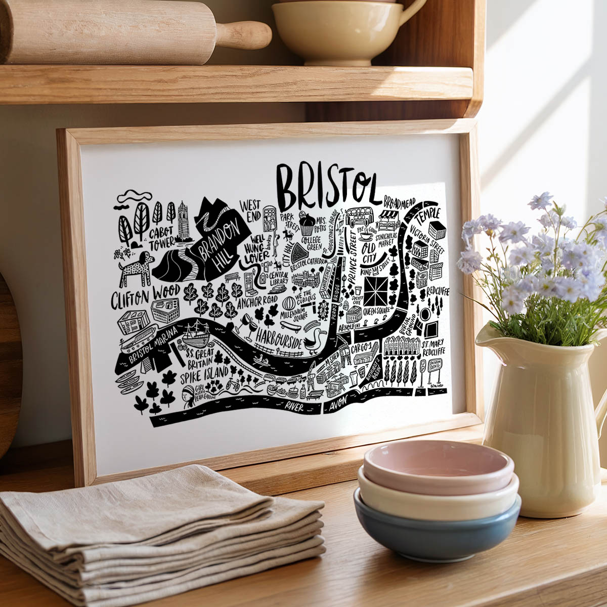 Framed map of Bristol on a kitchen counter with bowls and flowers.