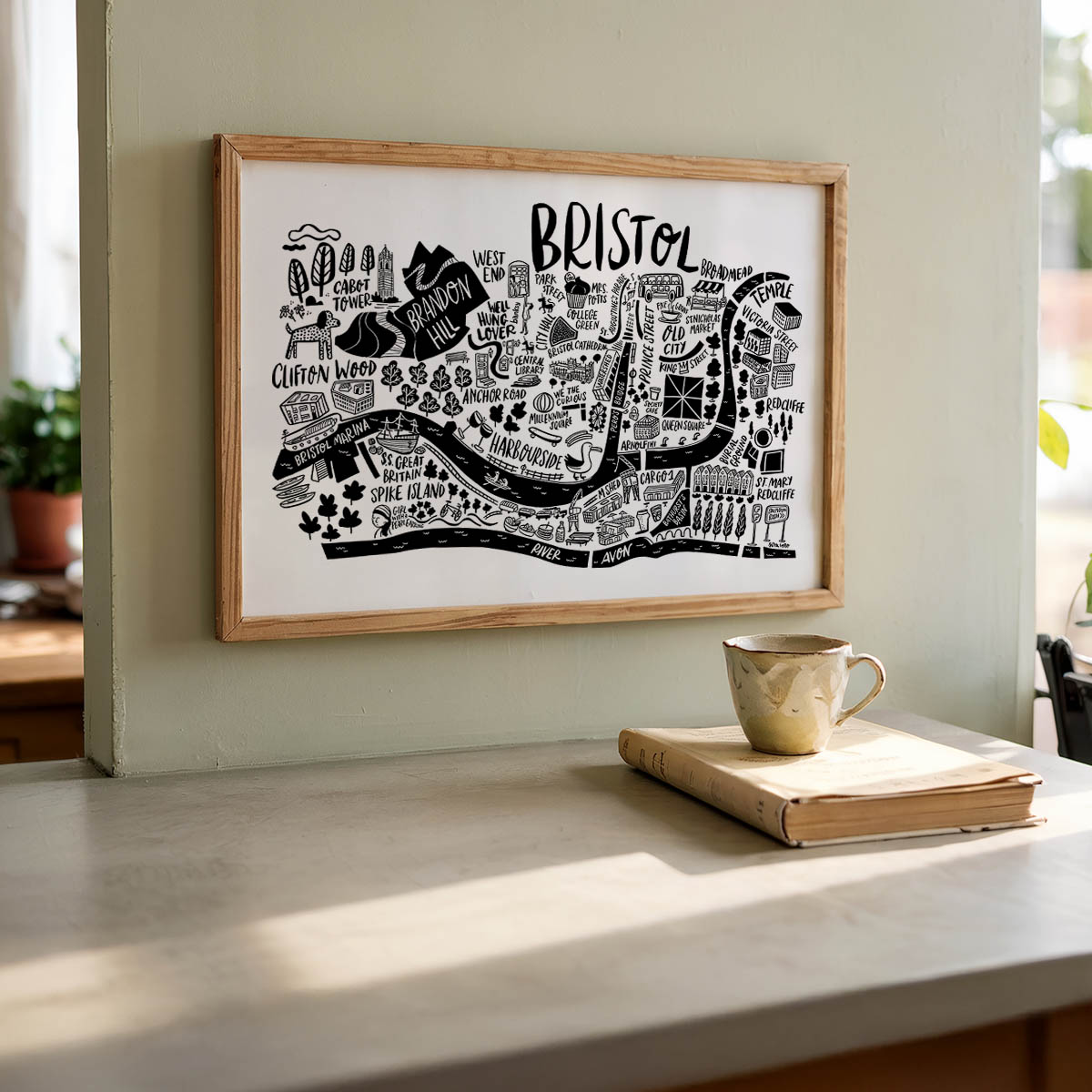 Framed map of Bristol on a wall above a table with a mug and book.