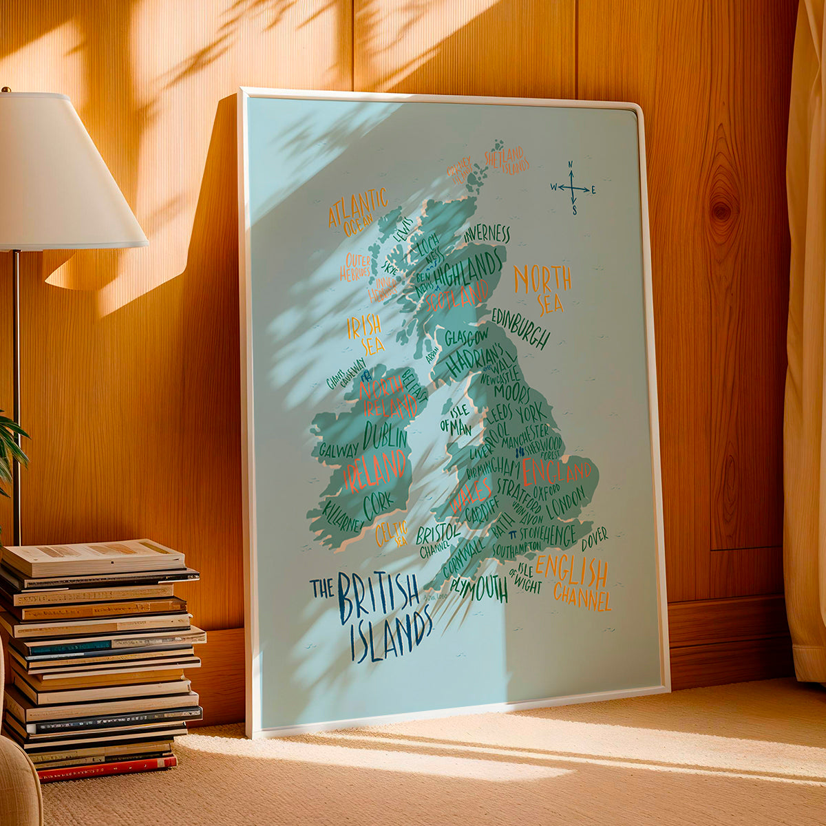 Framed map of the British Isles on a wooden surface with books and a lamp in the background