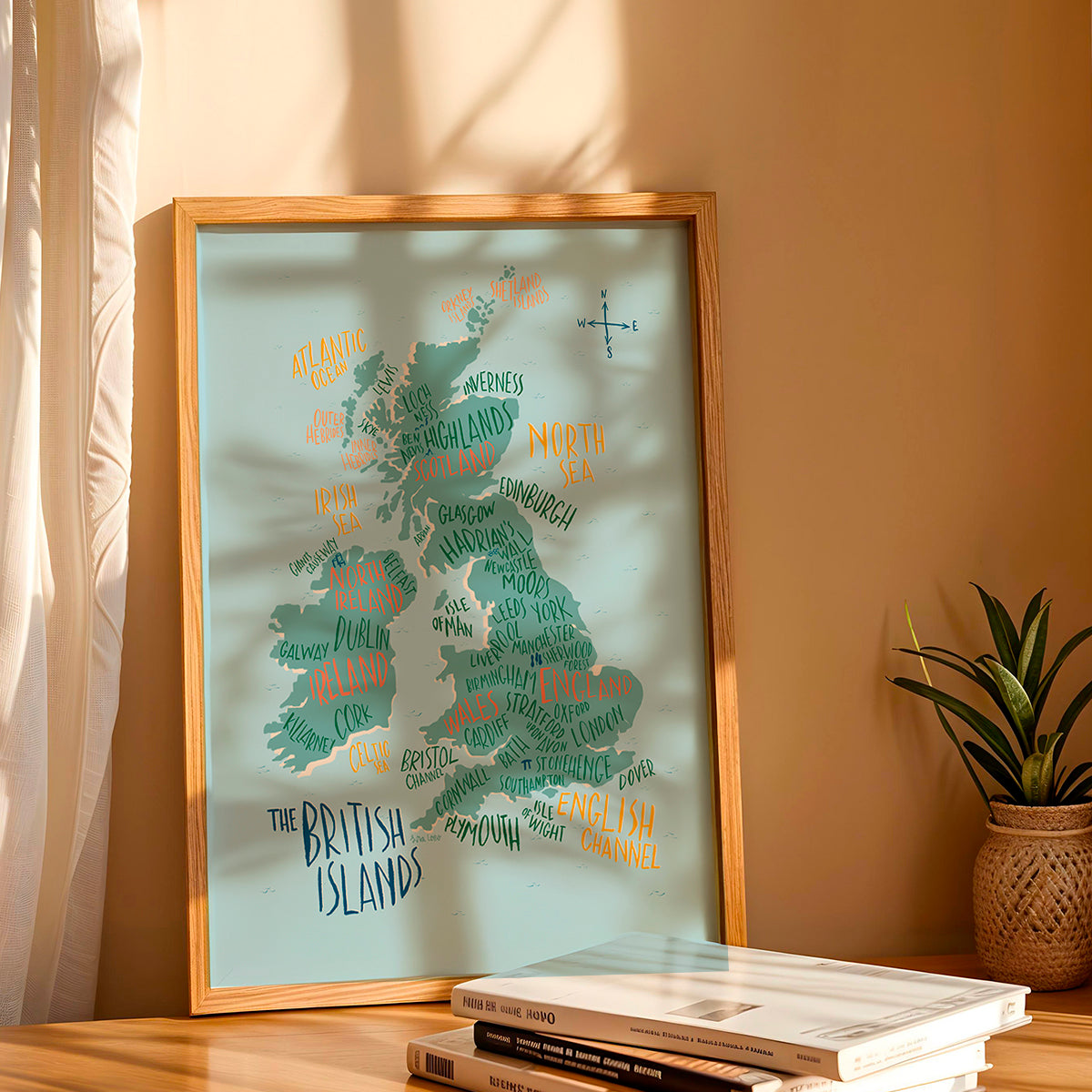 Framed map of the British Isles on a wooden surface with a plant and books in the background.