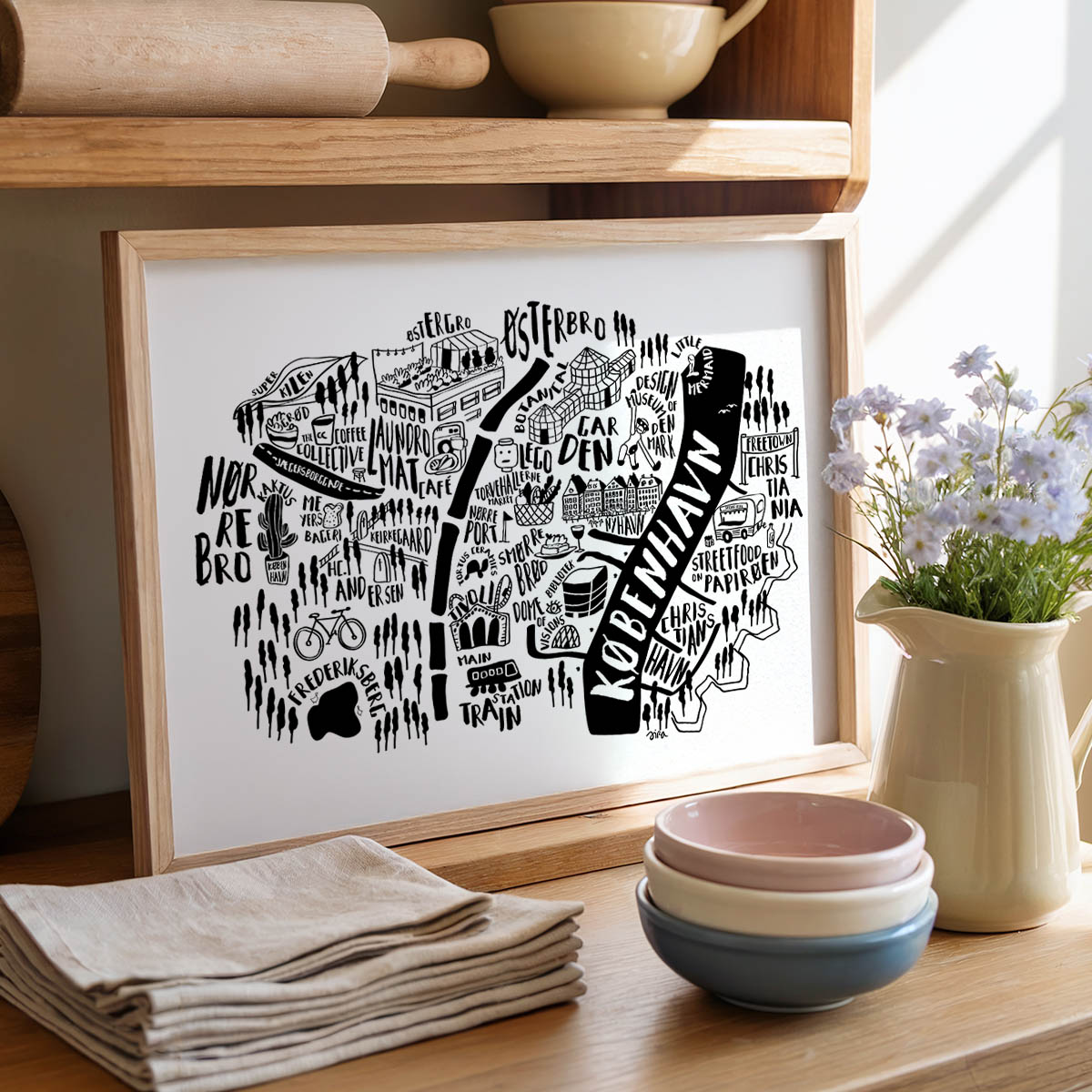 Framed black and white map print on a kitchen counter with bowls and flowers.