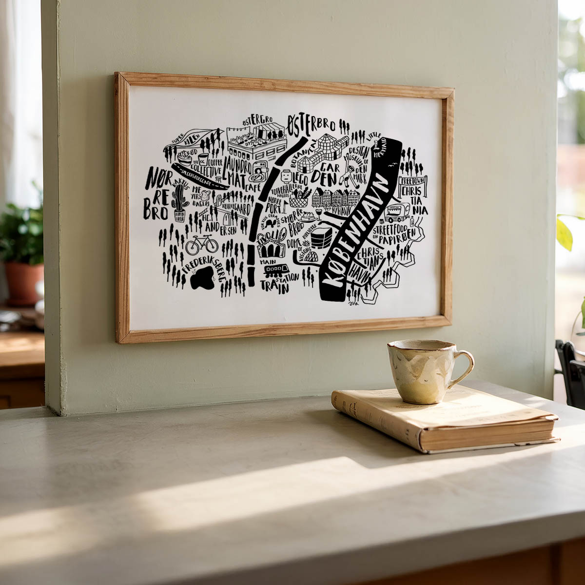 Framed map artwork on a wall above a table with a book and mug.