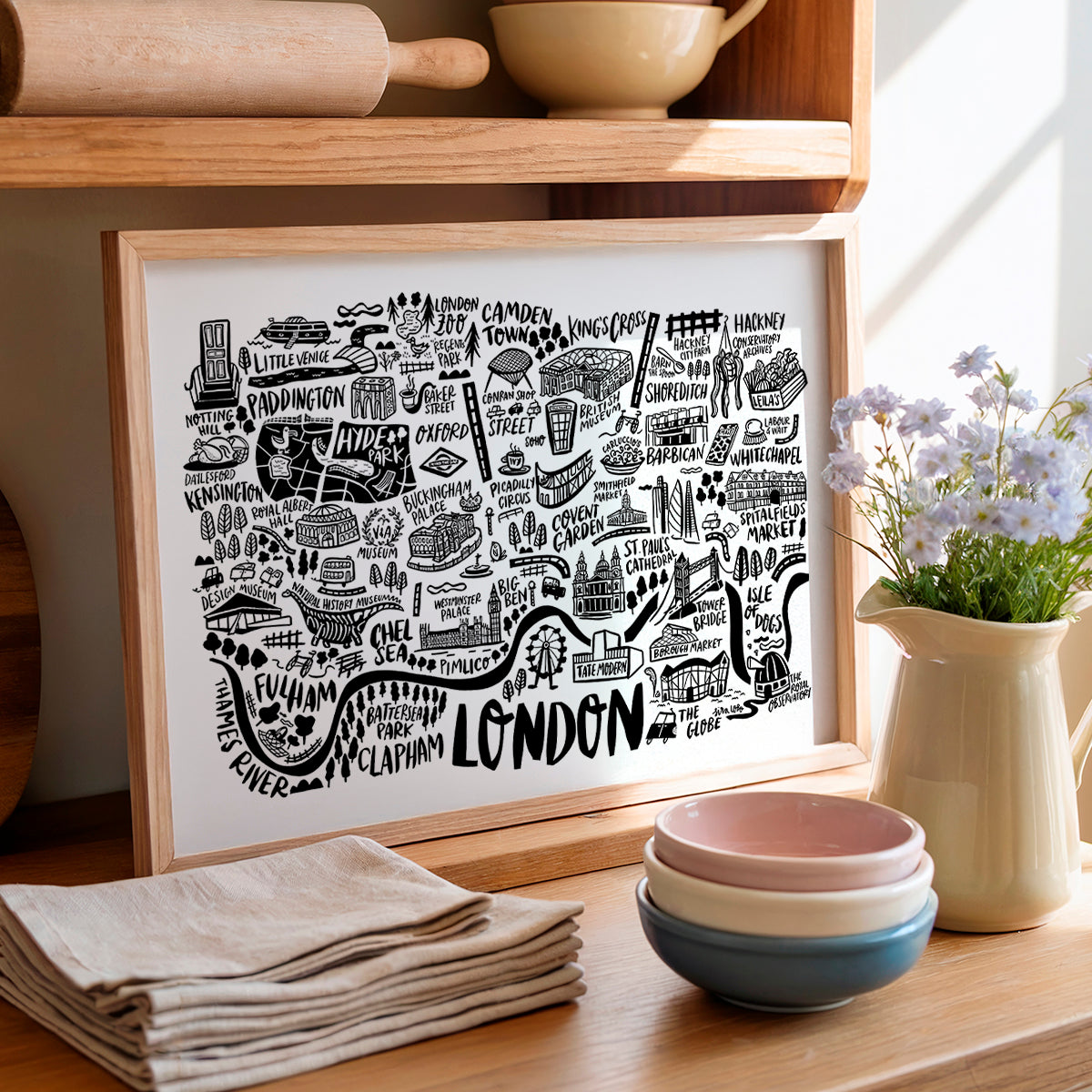 Framed map of London on a kitchen counter with bowls and flowers.