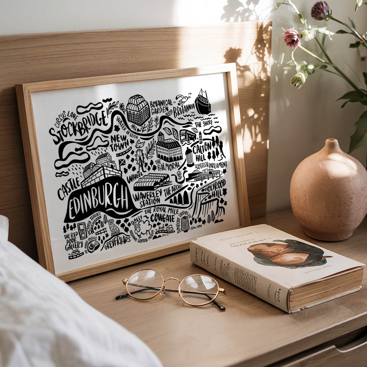 Framed map of Edinburgh on a wooden surface with a book and glasses.