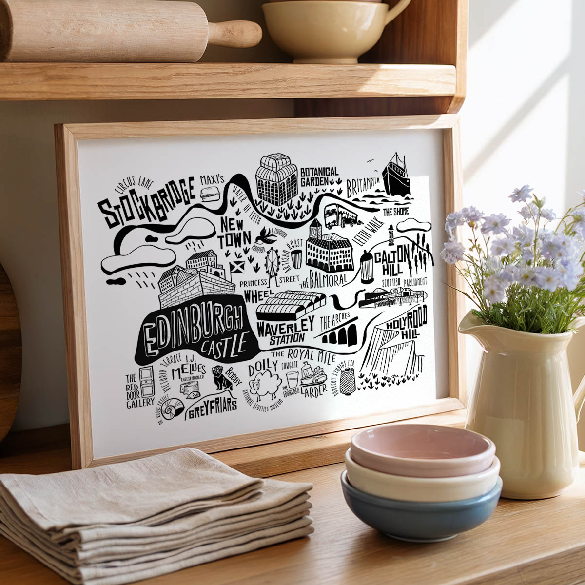 Framed map of Edinburgh on a wooden shelf with kitchen items and flowers.