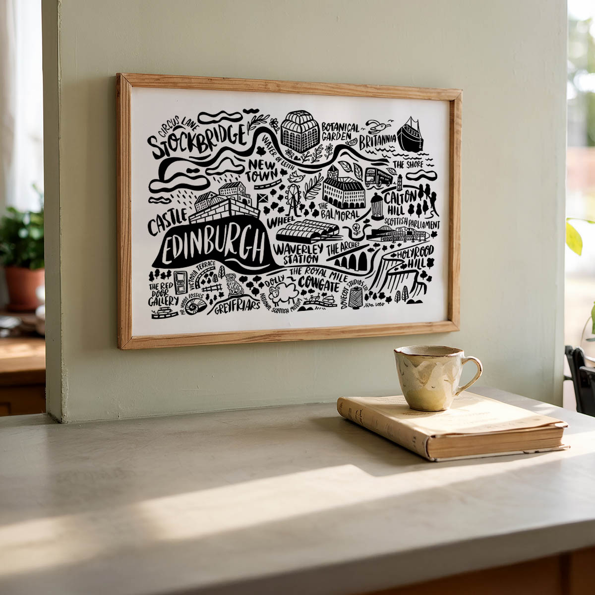 Framed map of Edinburgh on a wall with a cup and book on a table below.