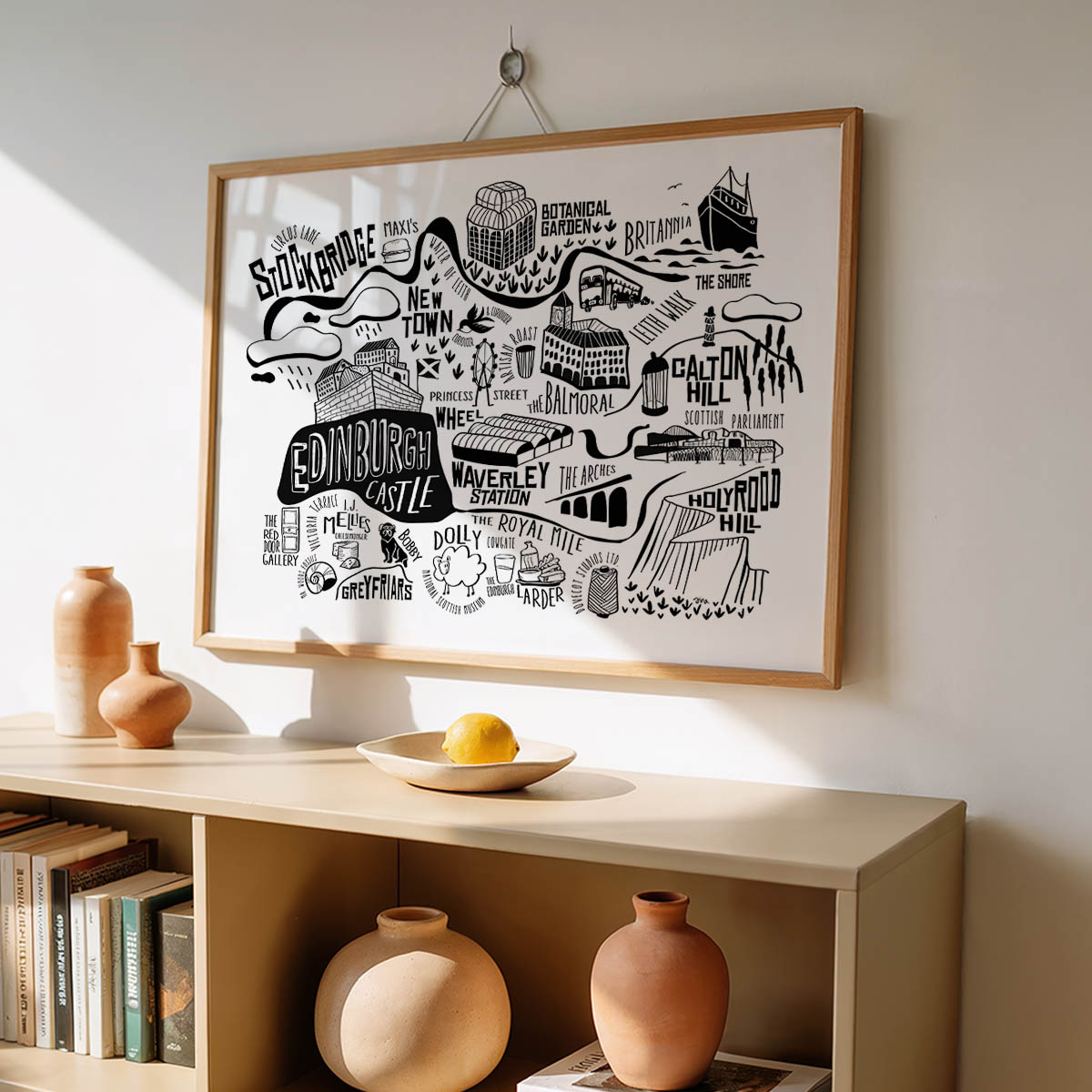 Framed black and white map of Edinburgh on a wall above a wooden shelf with decorative vases and books.