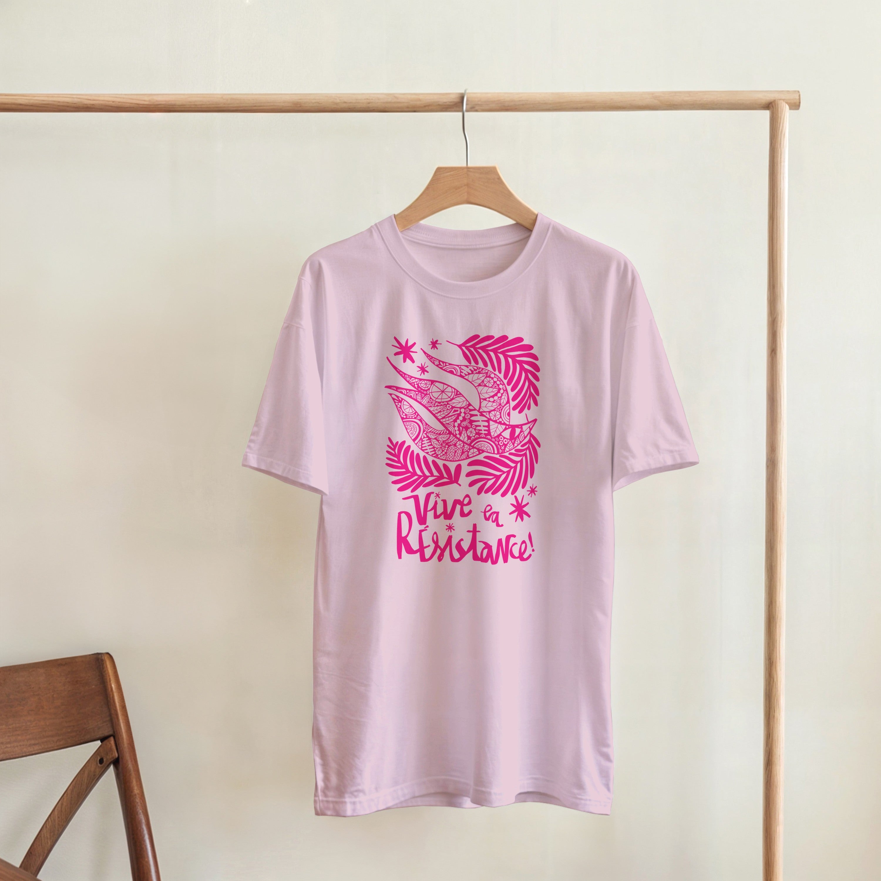 Pink t-shirt with a graphic design and text on a hanger against a plain background
