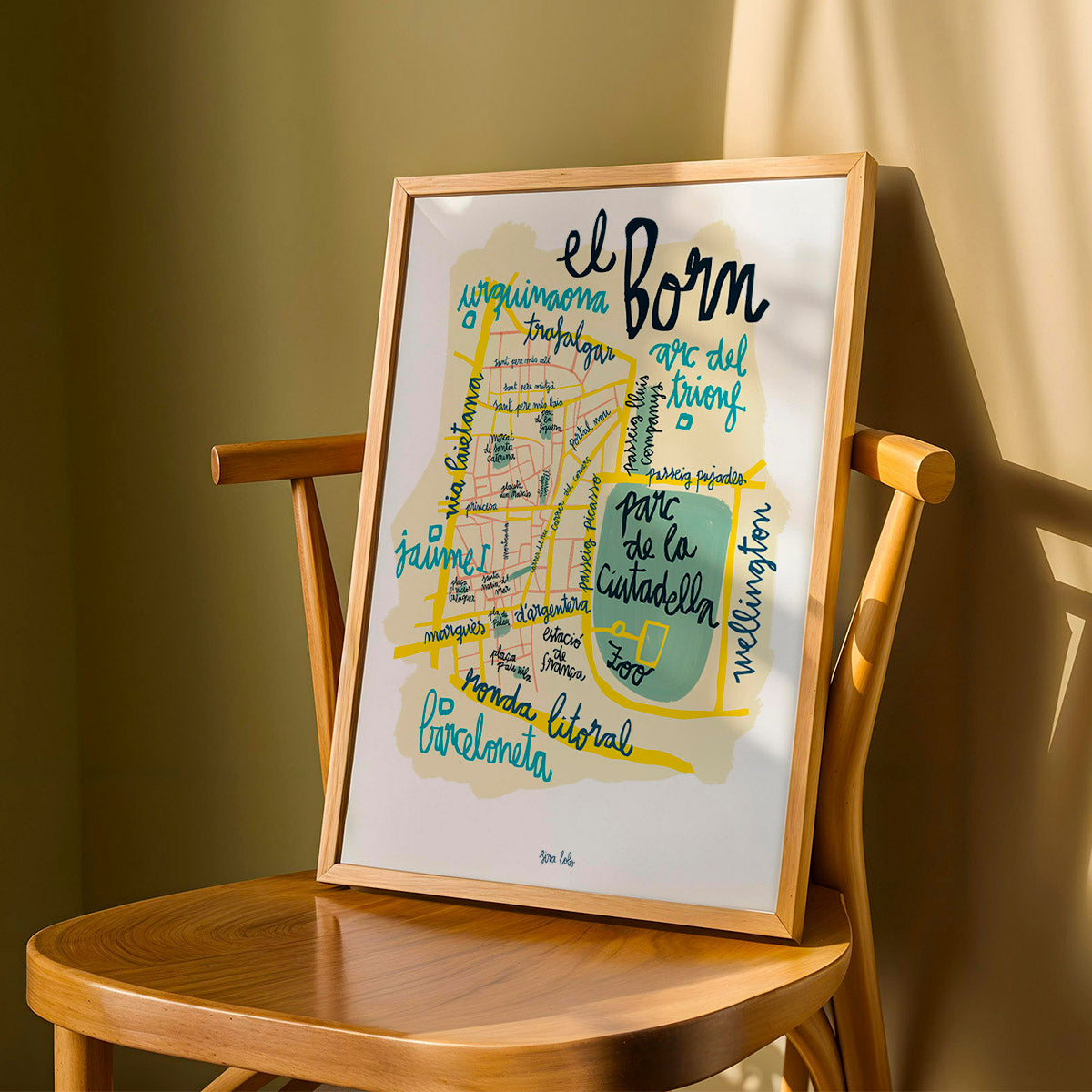 Framed map of El Born district in Barcelona on a wooden chair against a beige wall.
