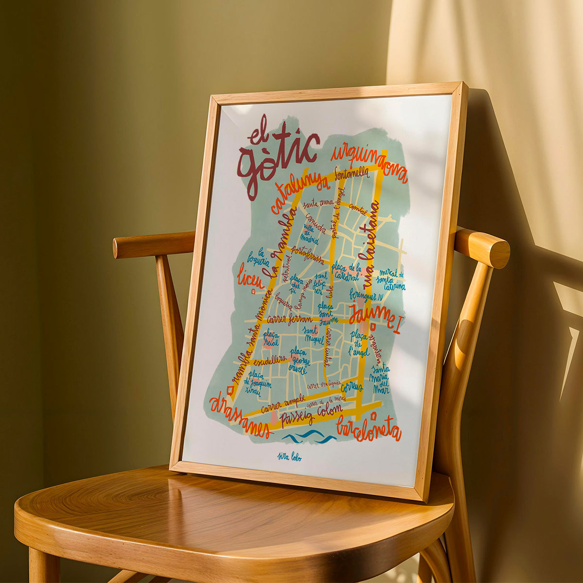 Framed map of Gotic area in Barcelona on a wooden chair against a green wall.