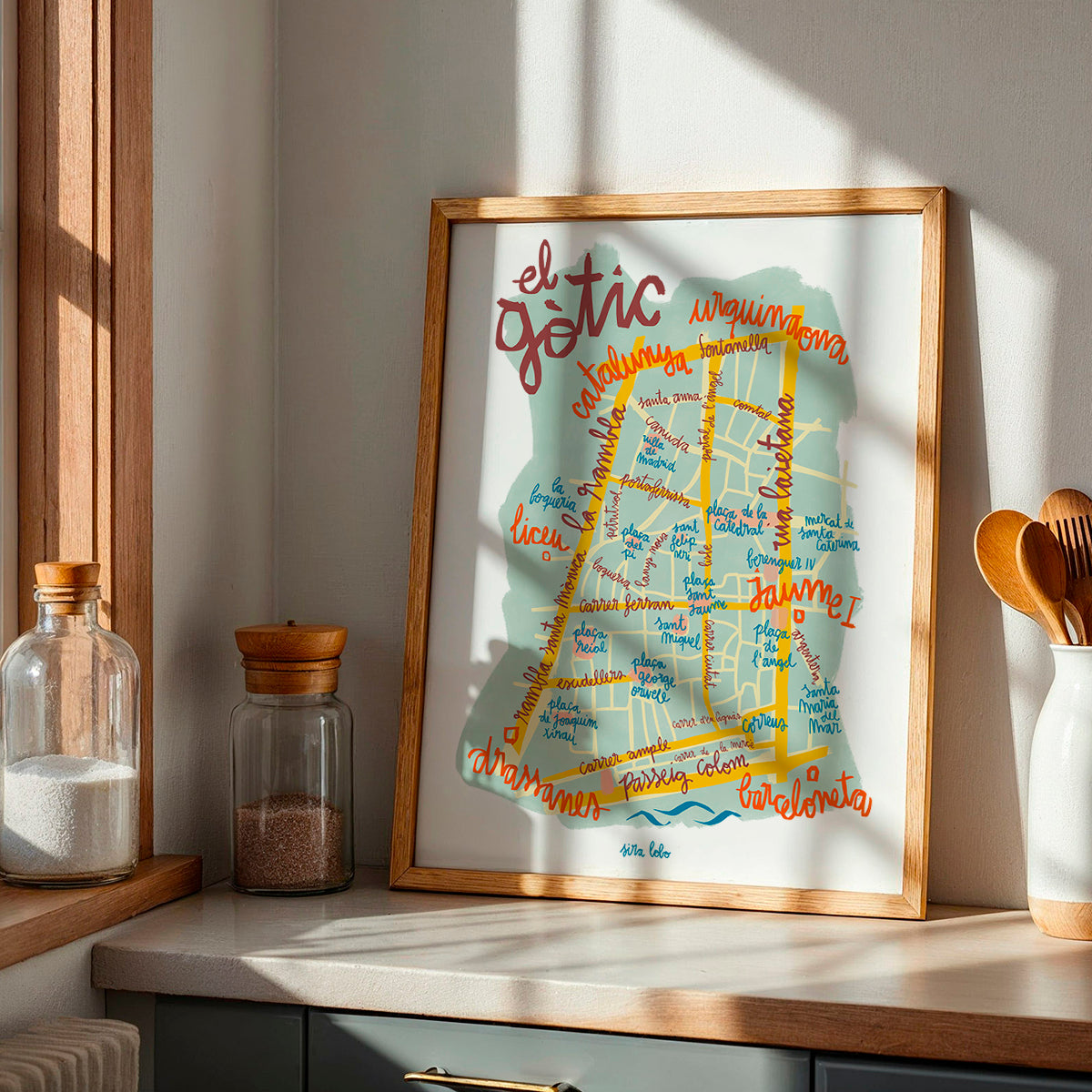 Framed map of El Gotic neighborhood in Barcelona on a kitchen counter with jars and utensils.