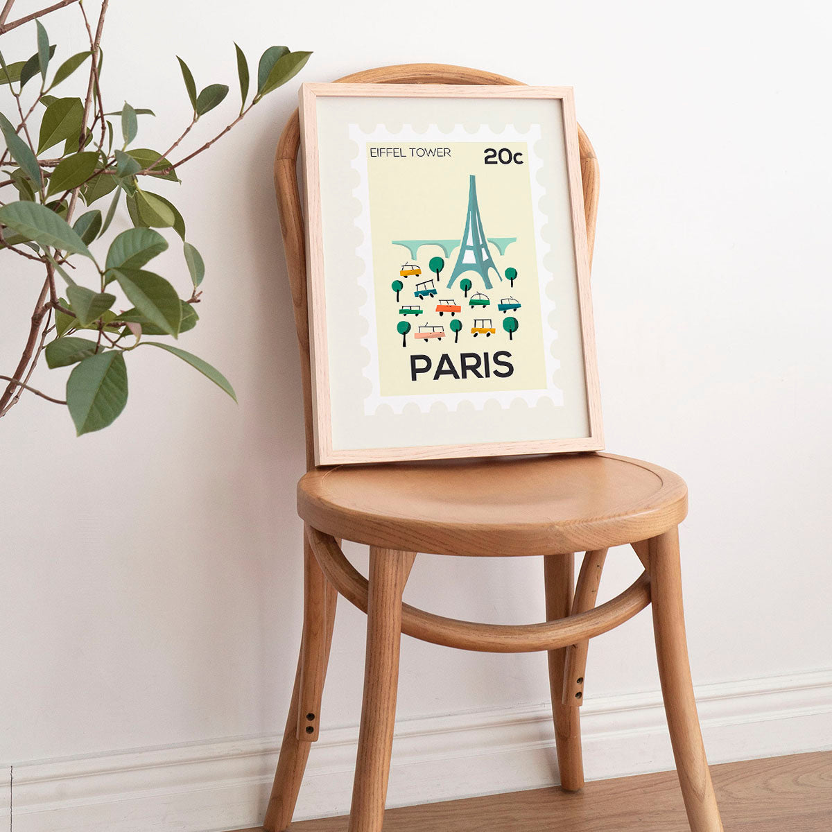 Framed poster of the Eiffel Tower on a wooden chair with a plant in the background